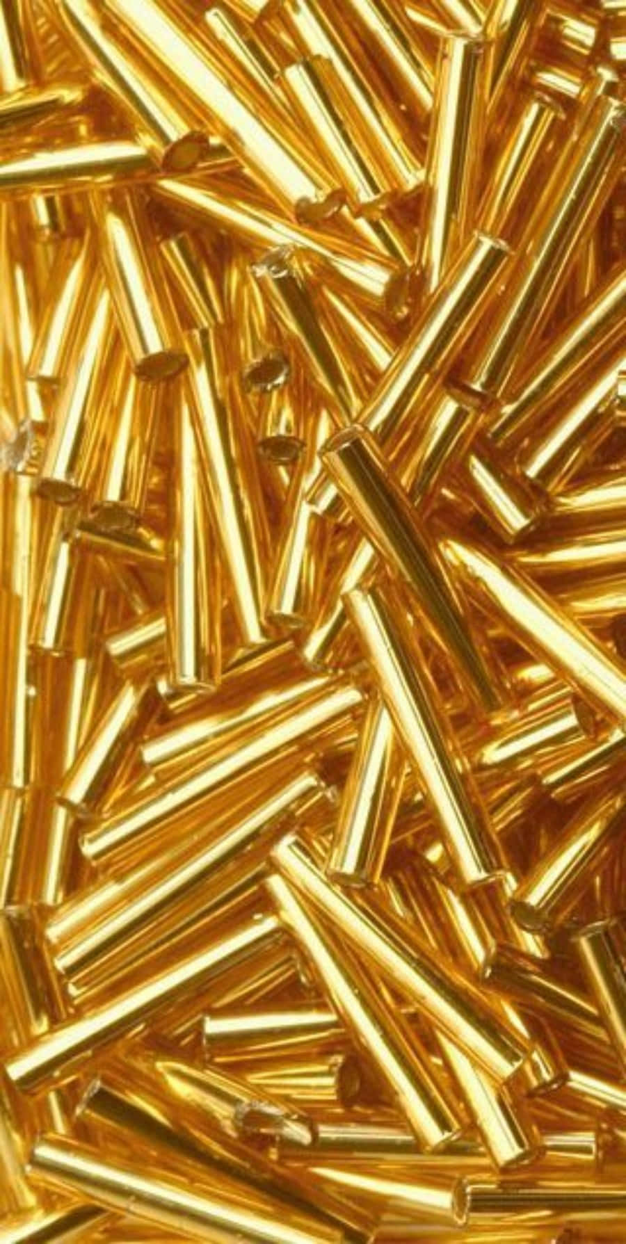 金色機遇 壁紙 — 密集特寫鏡頭，展示閃亮金色圓柱形珠子以混亂、反射性排列散落。