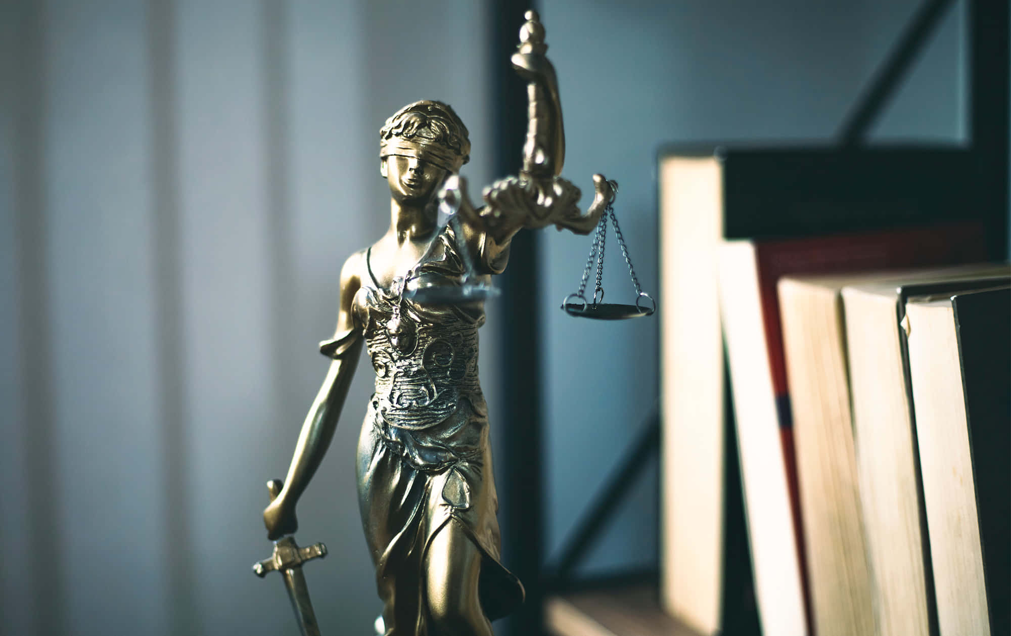 Justice 桌布 壁紙 — 金色正義女神雕像手持天秤與劍，立於柔和光線的辦公室環境中，旁邊有書本。