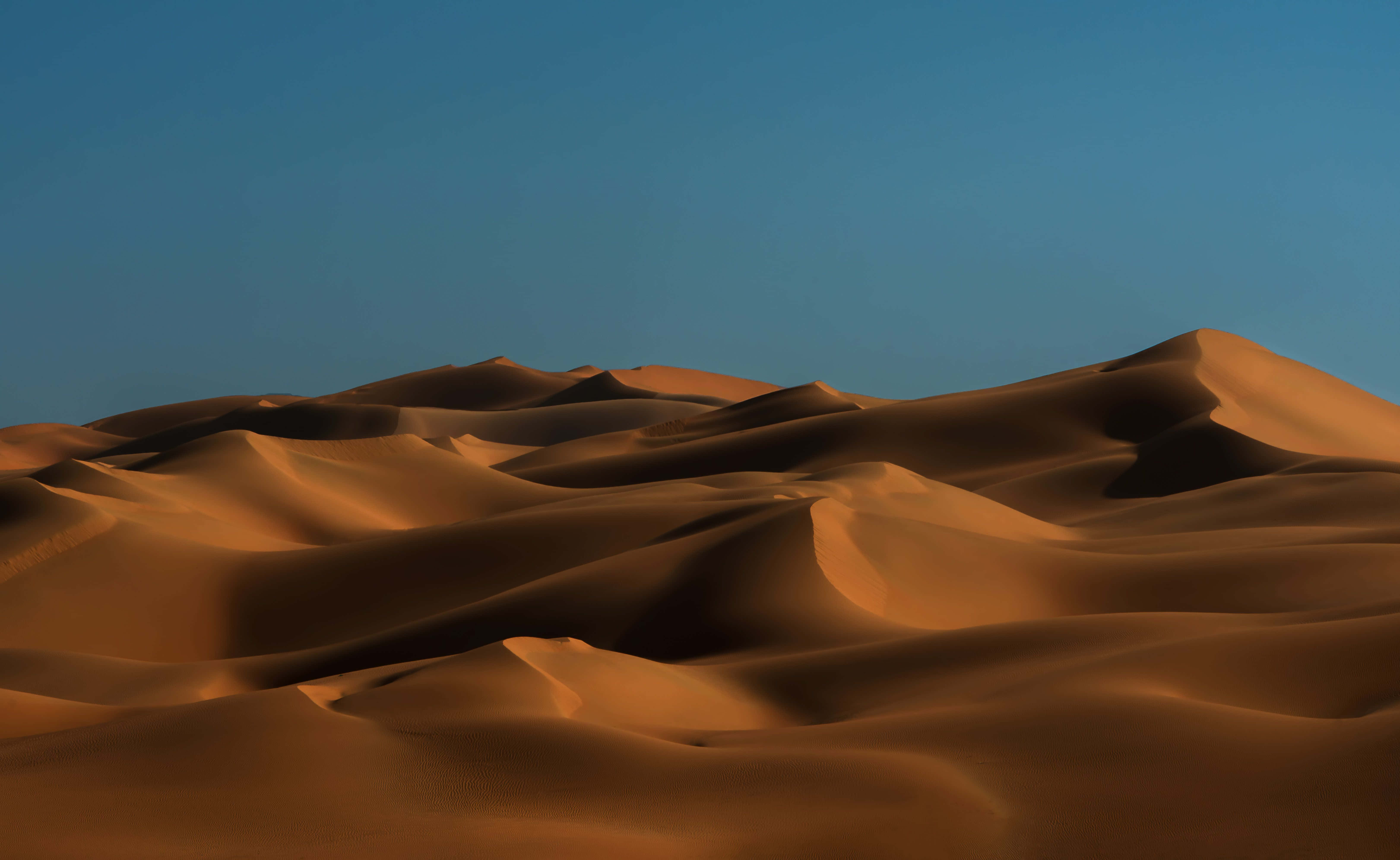 Uae 桌布 壁紙 — 金色沙丘在廣闊的沙漠景觀中，在清澈的藍天下起伏。
