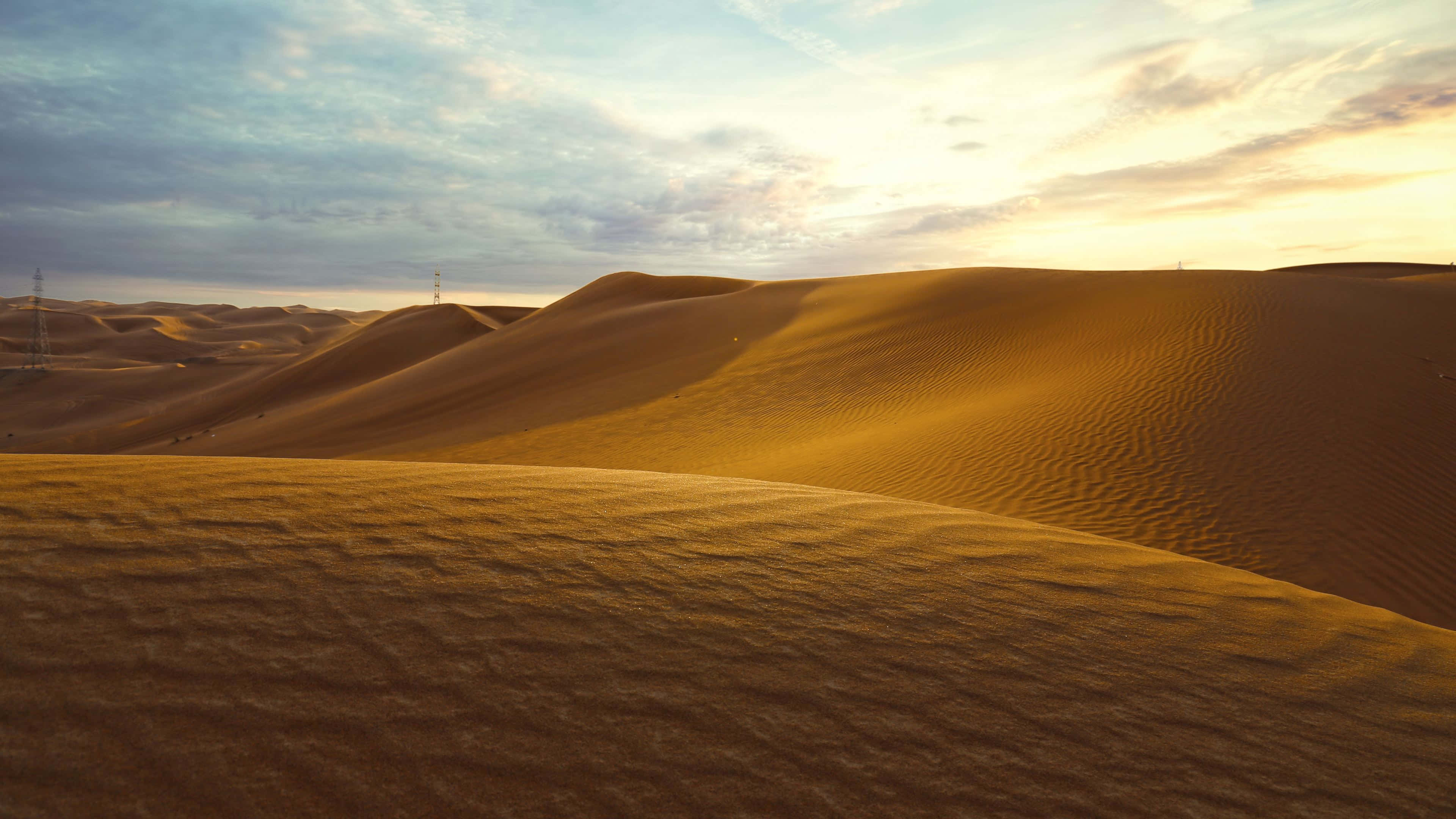 Sand Dunes 桌布 壁紙 — 金色沙丘在柔和嘅日落天空下起伏，有零星雲朵同遠處嘅電線。
