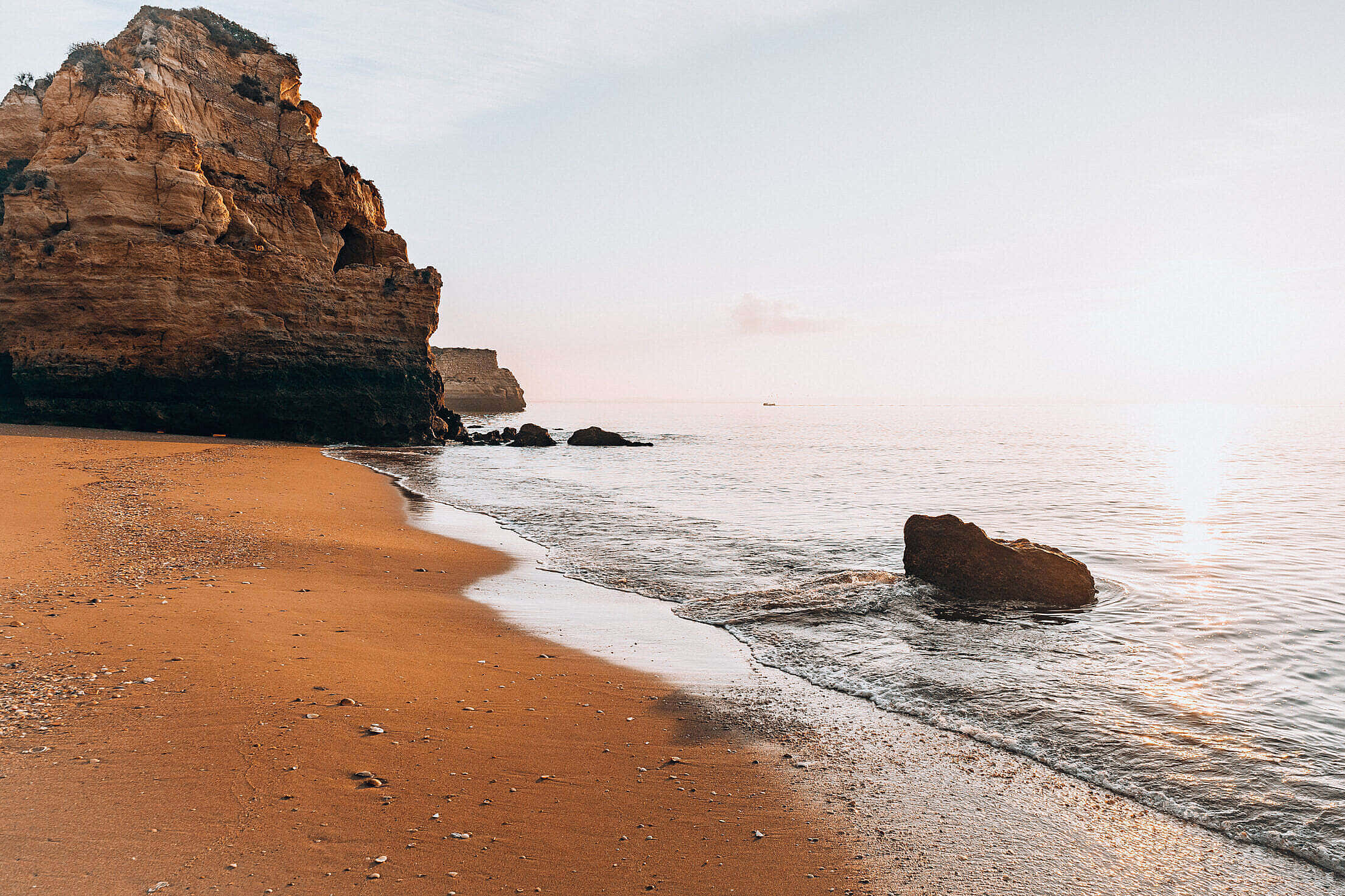 Portuguese Beach 桌布 壁紙 — 金色沙灘與平靜的海面在日出時相遇，崎嶇的懸崖投下長長的影子。