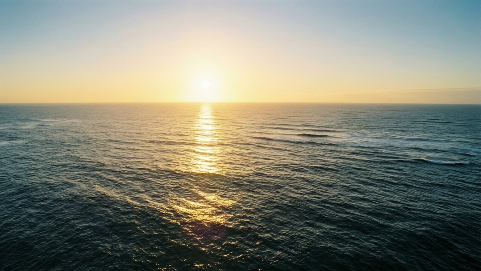金色海洋日出 壁紙 — 晴朗藍天下，金色日出映照在平靜海浪上的鳥瞰圖。