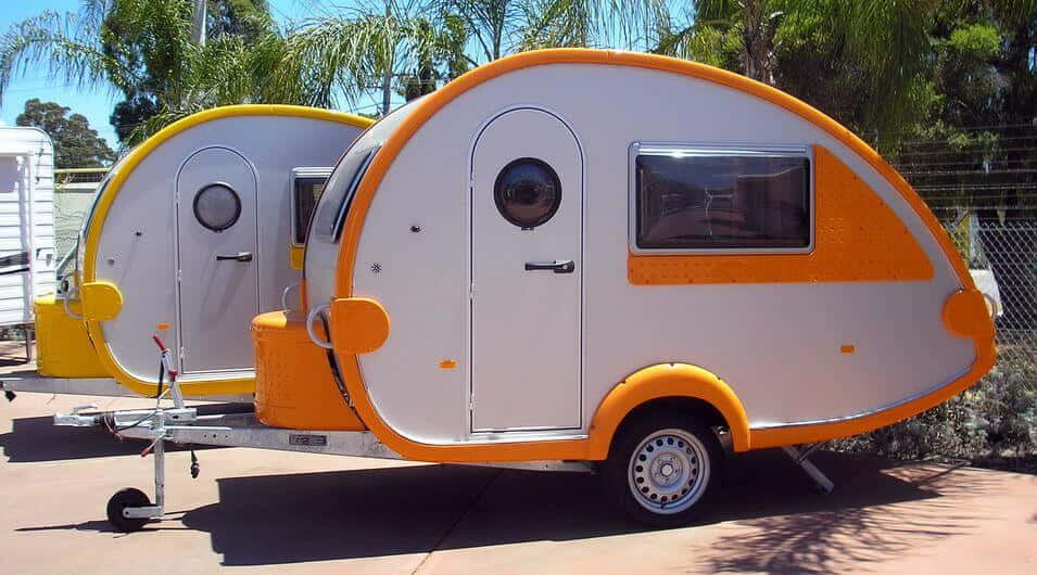 金色海灘上的陽光露營車 壁紙 — 兩輛帶有白色和橙色裝飾的復古水滴形拖車在陽光明媚的日子裡停放在棕櫚樹下。