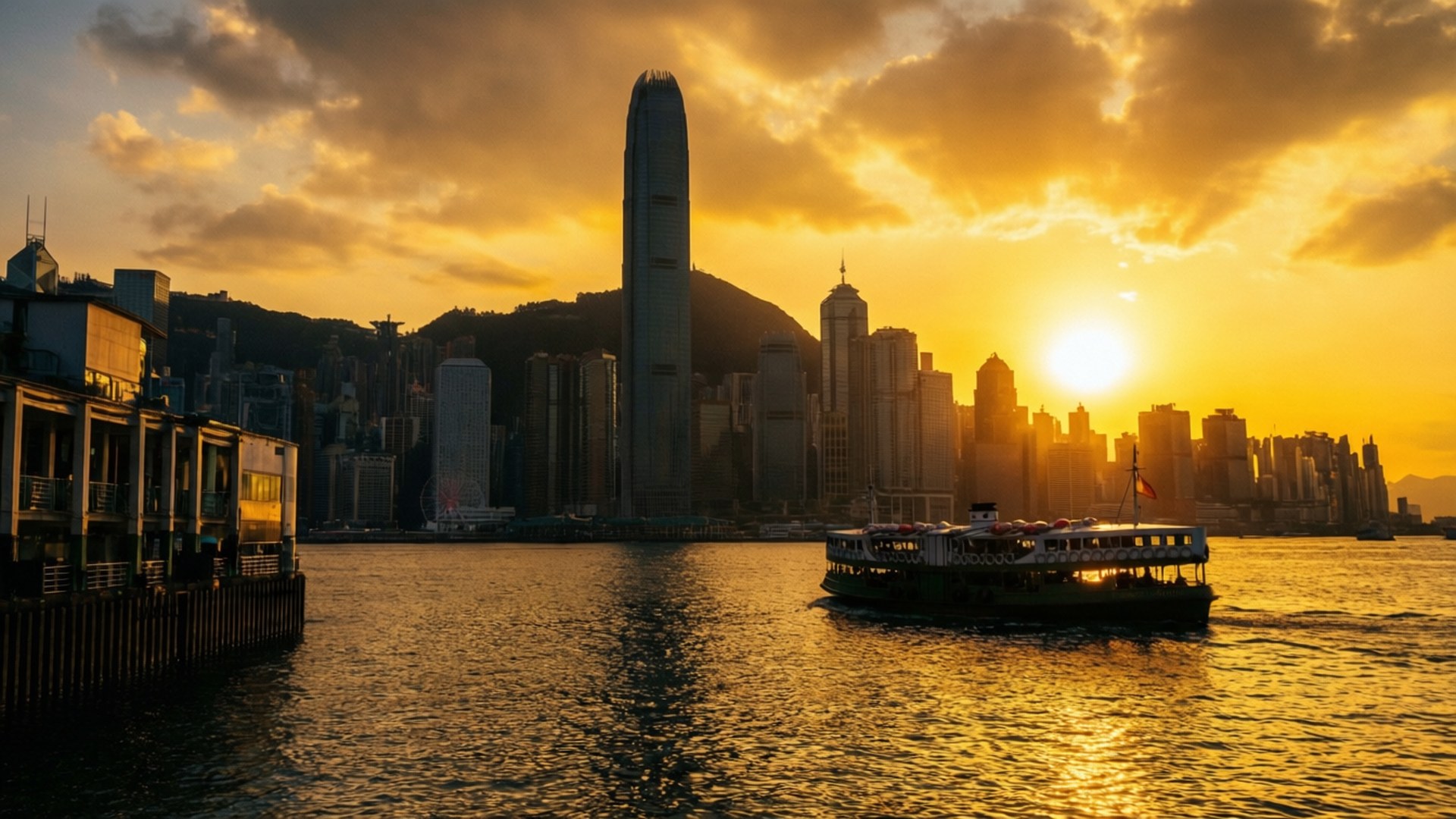 金色港口日落 壁紙 — 一艘渡輪在日落時分，於香港高聳的天際線和戲劇性的雲層下，滑過金色的水域。