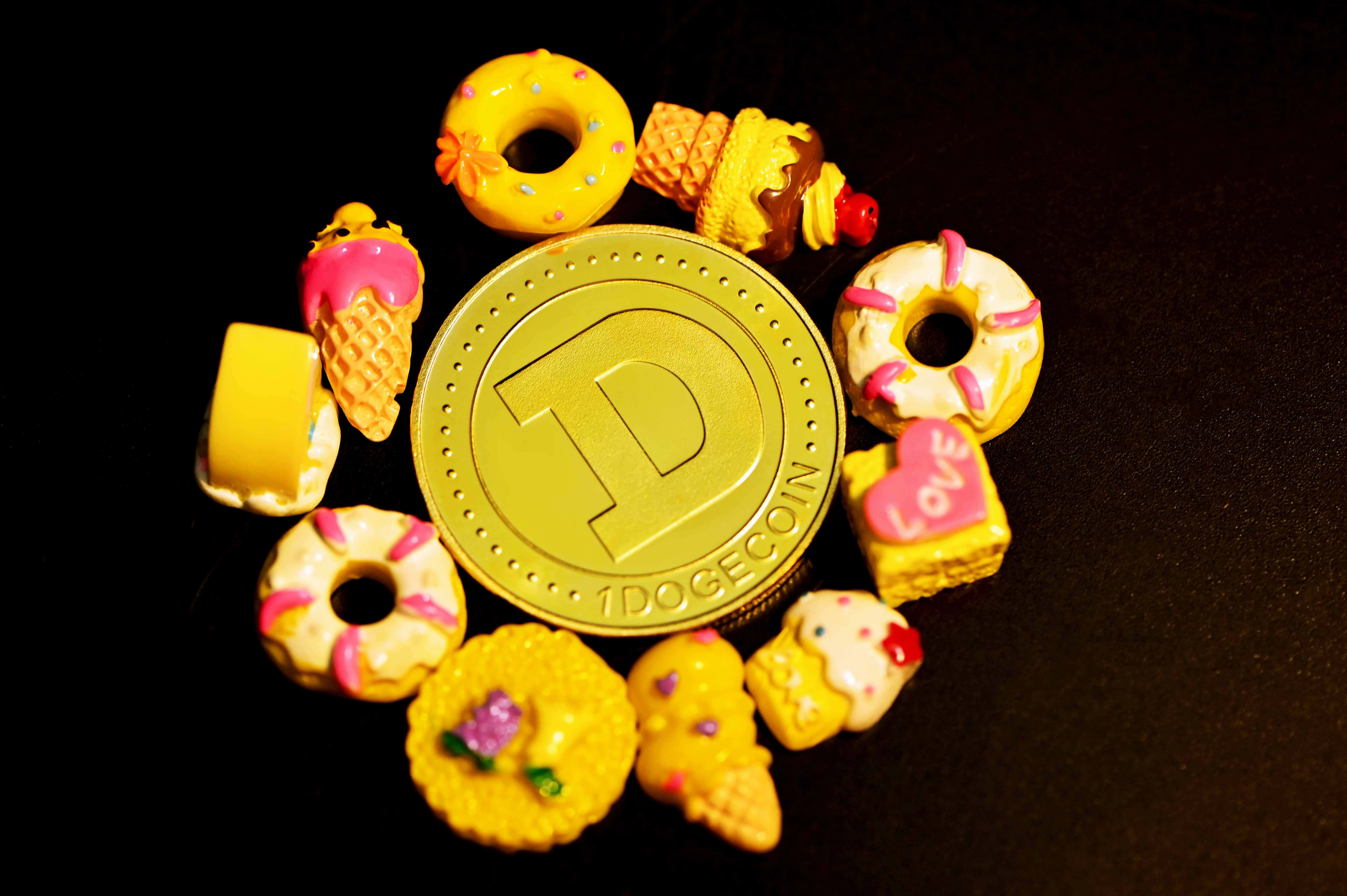 Dogecoin 桌布 壁紙 — 金色狗狗幣被色彩繽紛的微型甜品飾物包圍在黑色背景上。