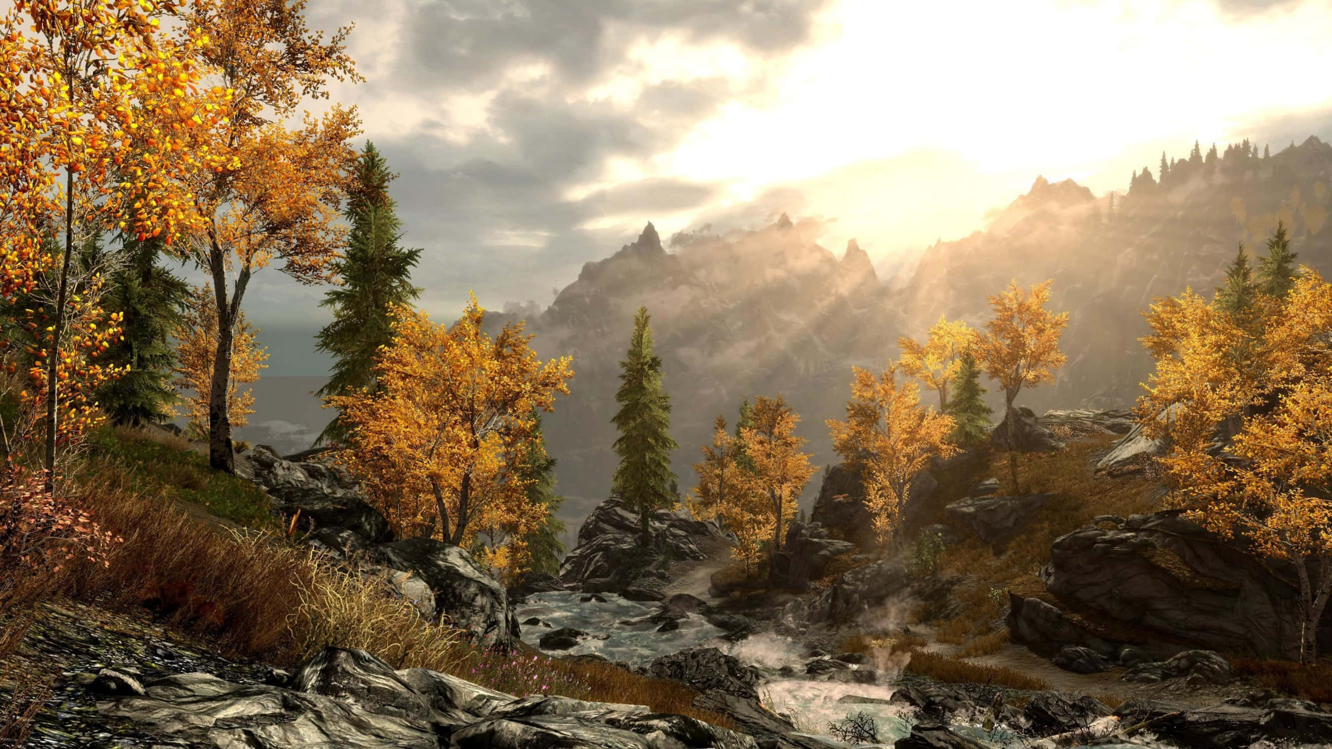 Skyrim Landscapes 桌布 壁紙 — 金色的秋樹點綴著岩石地形，陽光穿過雲層照射在霧氣繚繞的山巒之上。