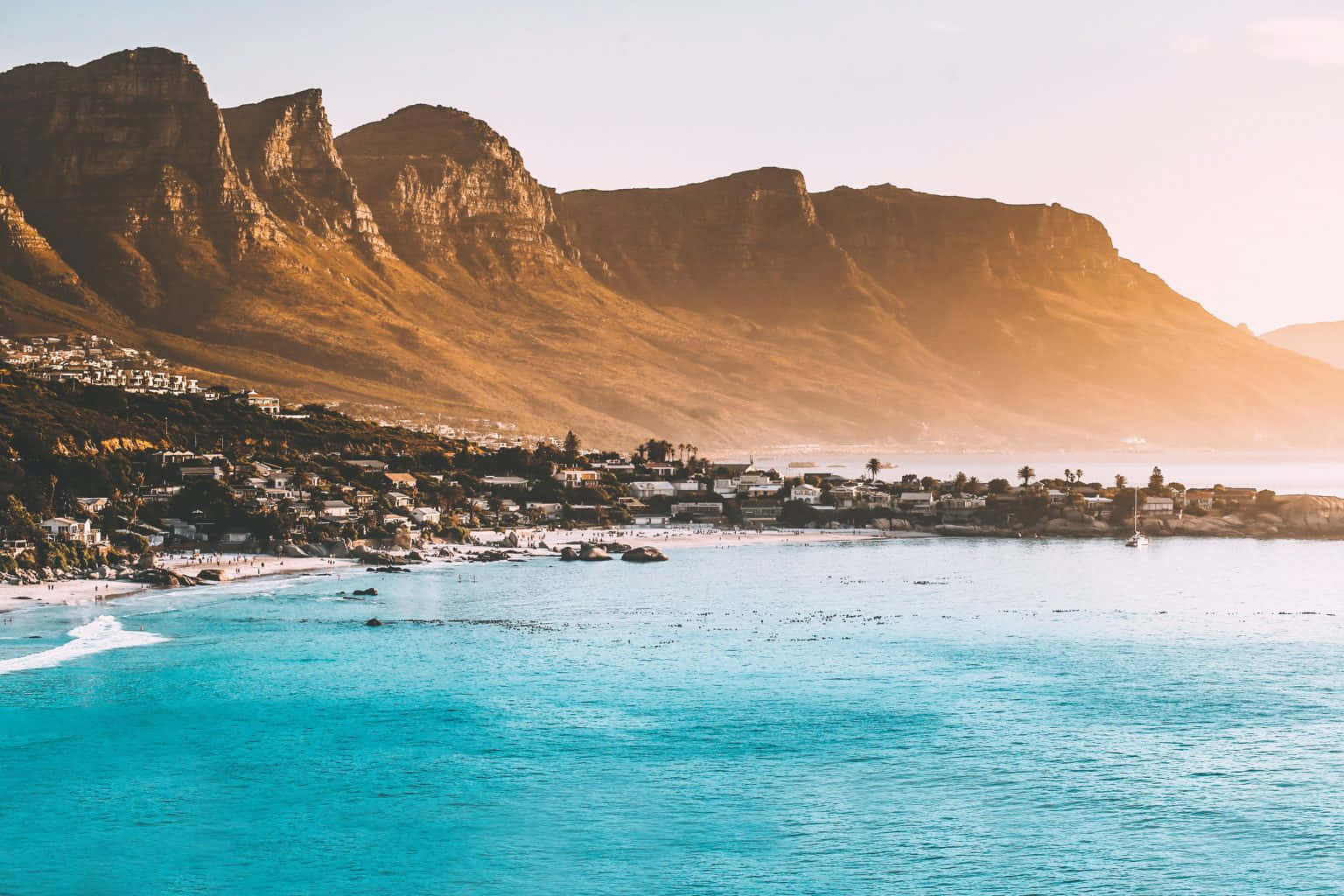 South Africa 桌布 壁紙 — 金色的陽光灑在桌山的崎嶇懸崖上，而碧綠的海水在日落時分輕拍著沿海小鎮。