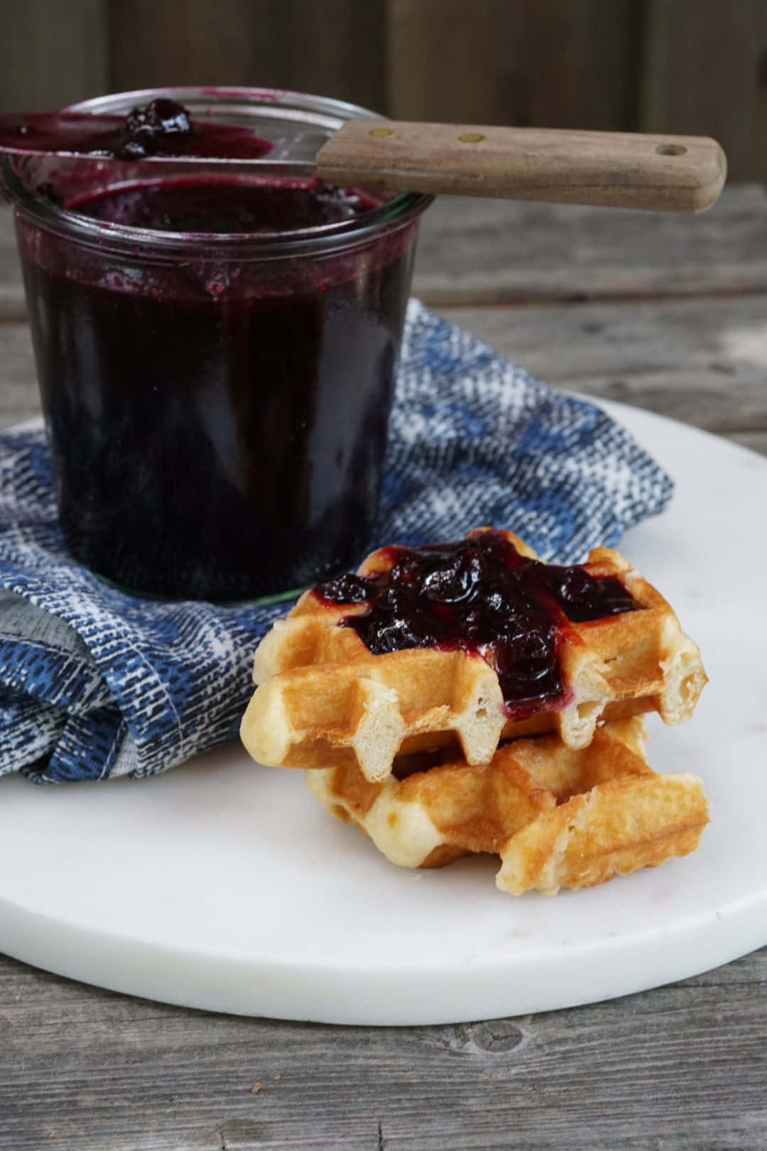 Blueberry Jam 桌布 壁紙 — 金色窩夫疊起配深色莓果醬，旁邊有玻璃罐，放在大理石碟上，鋪有藍色布。