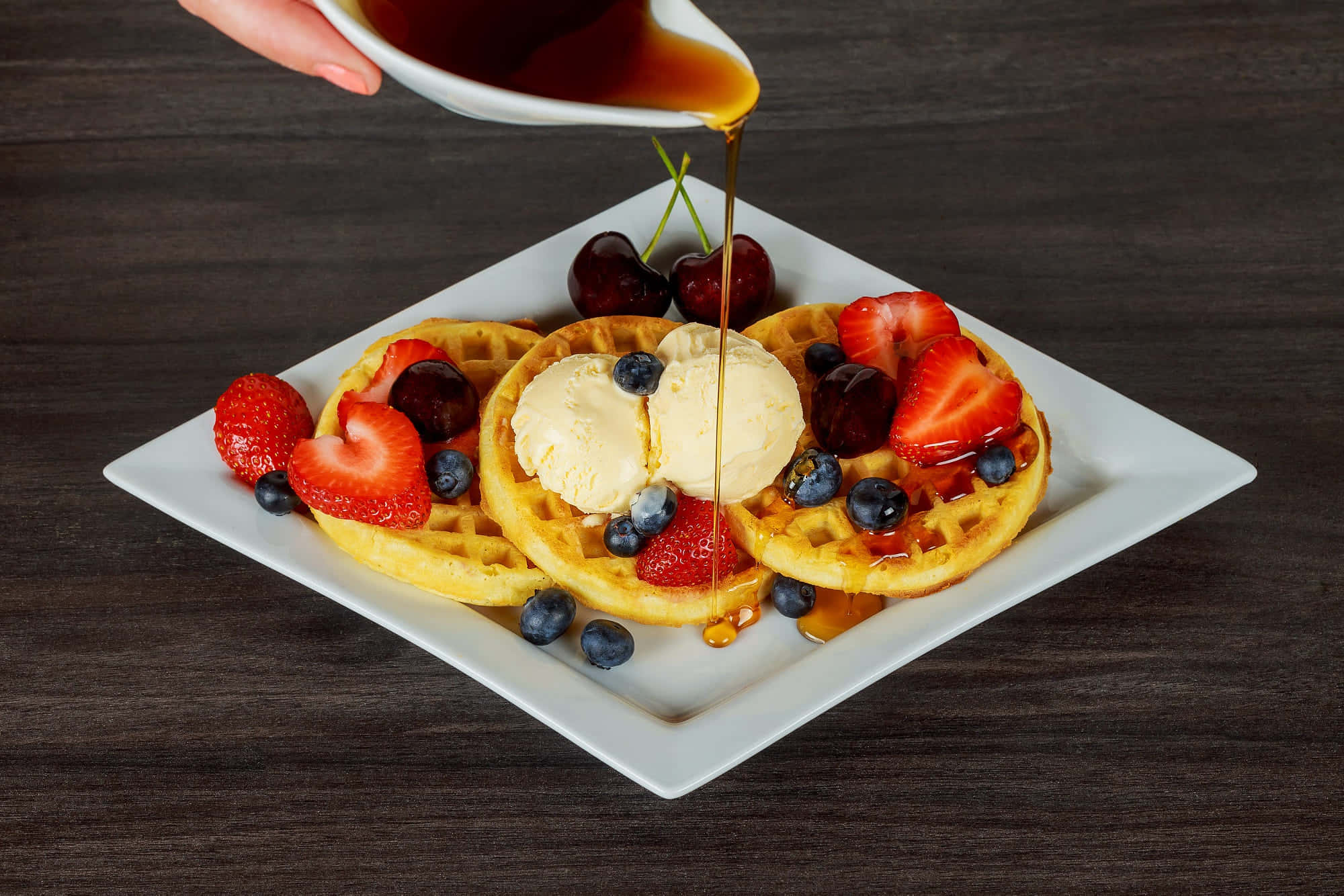 Waffle 桌布 壁紙 — 金色窩夫配上雪糕、新鮮莓果，並從白色壺中倒出糖漿在深色木桌上。