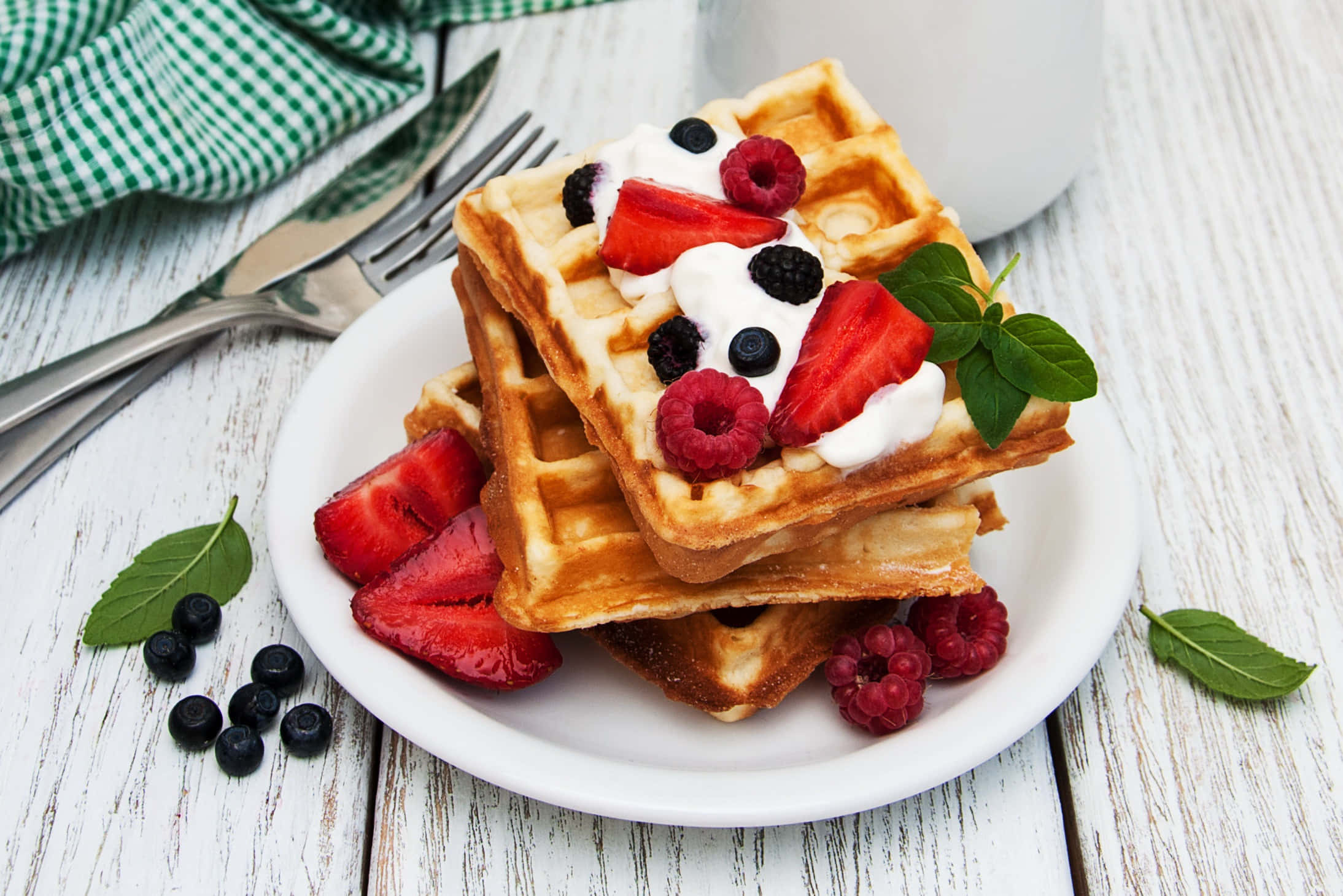 Waffle 桌布 壁紙 — 金色窩夫高高疊起，配上新鮮漿果、忌廉和薄荷，放在質樸的白色木桌上。