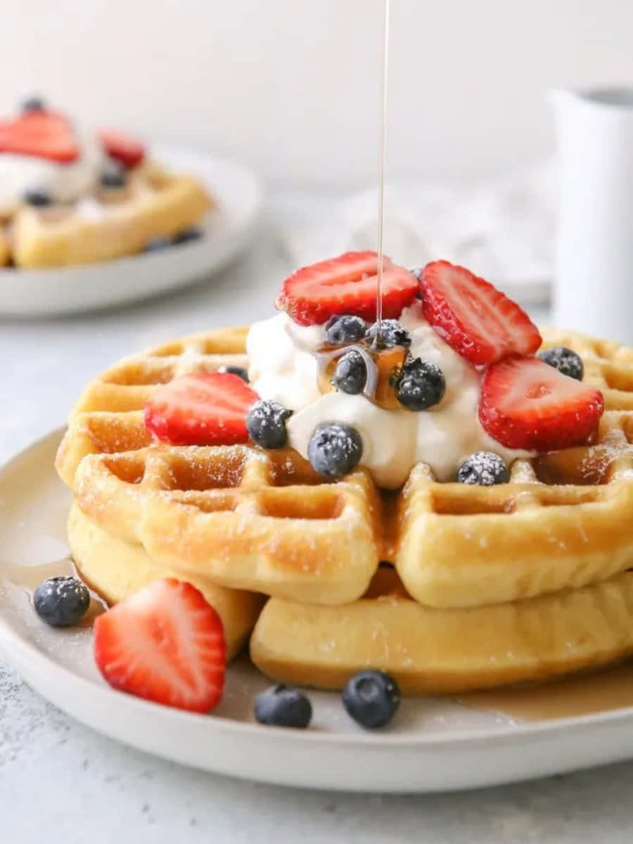 Waffle 桌布 壁紙 — 金色窩夫高高疊起，配上新鮮草莓、藍莓和忌廉，糖漿滴落，營造甜蜜的早餐場景。