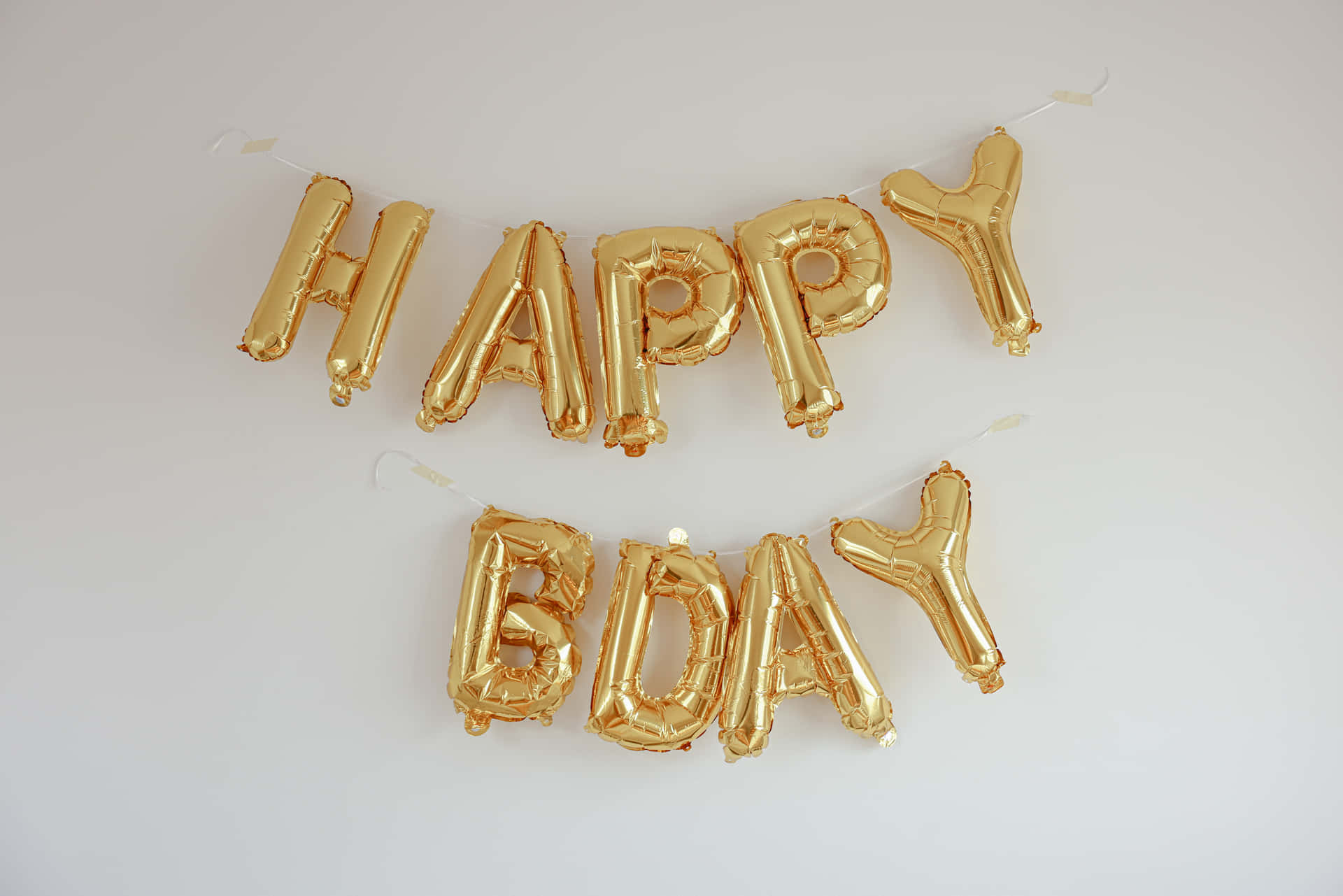 白色牆上金色生日氣球拼出 HAPPY BDAY。