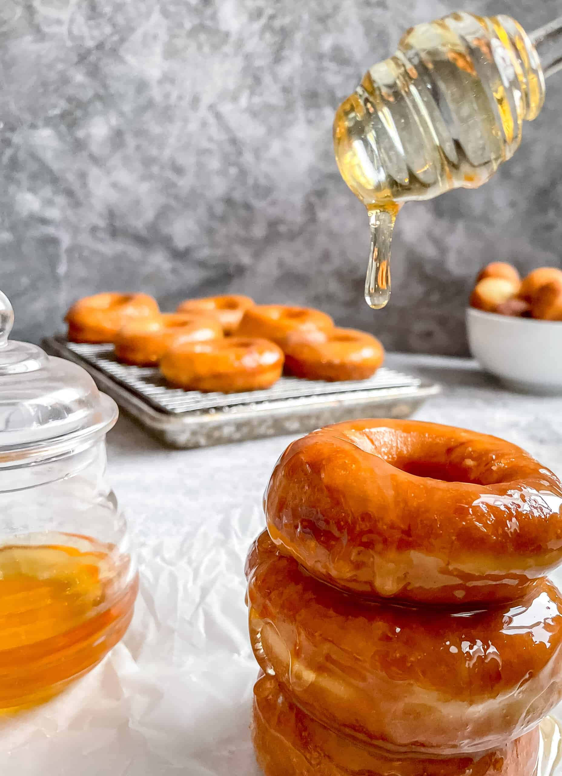 Glazed Donut 桌布 壁紙 — 金色糖霜冬甩高高疊起，蜂蜜從木勺滴落，背景為灰色大理石。