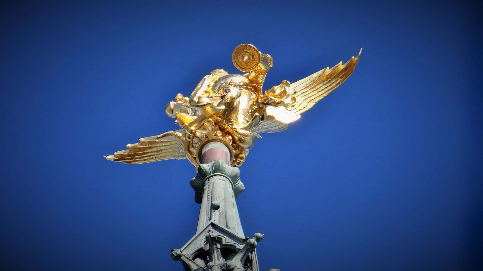 Saint Michael 桌布 壁紙 — 金色翅膀天使雕像立於華麗柱子上，背景是鮮豔的藍天。