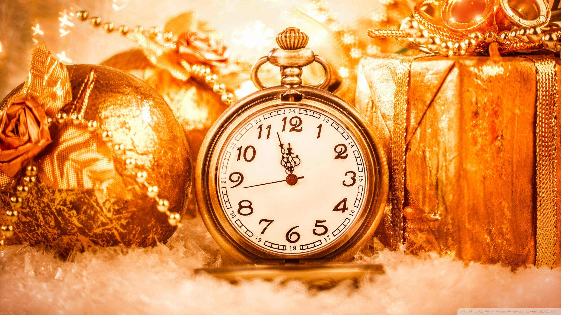 金色聖誕懷錶 壁紙 — 金色懷錶放在雪地上，旁邊有包裝好的禮物和裝飾品，在節日燈光下溫暖地閃耀。