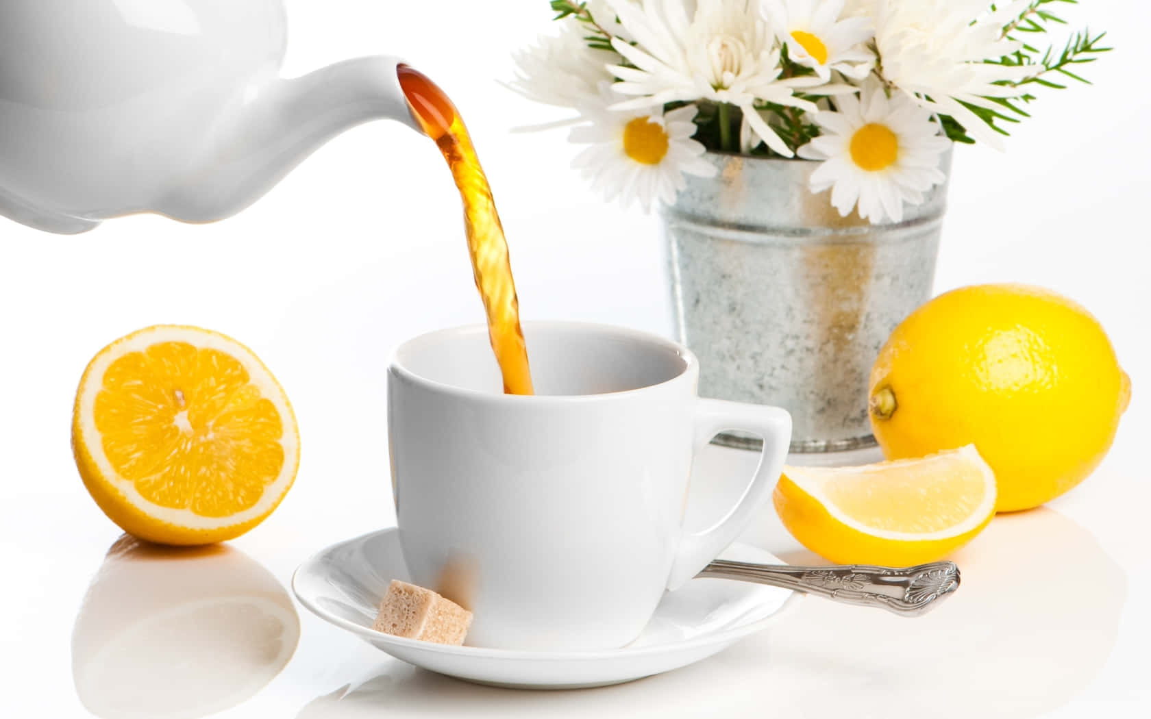 Floral Tea 桌布 壁紙 — 金色茶從白色水壺倒入杯中，旁邊有新鮮檸檬和鄉村風格桶中的雛菊。