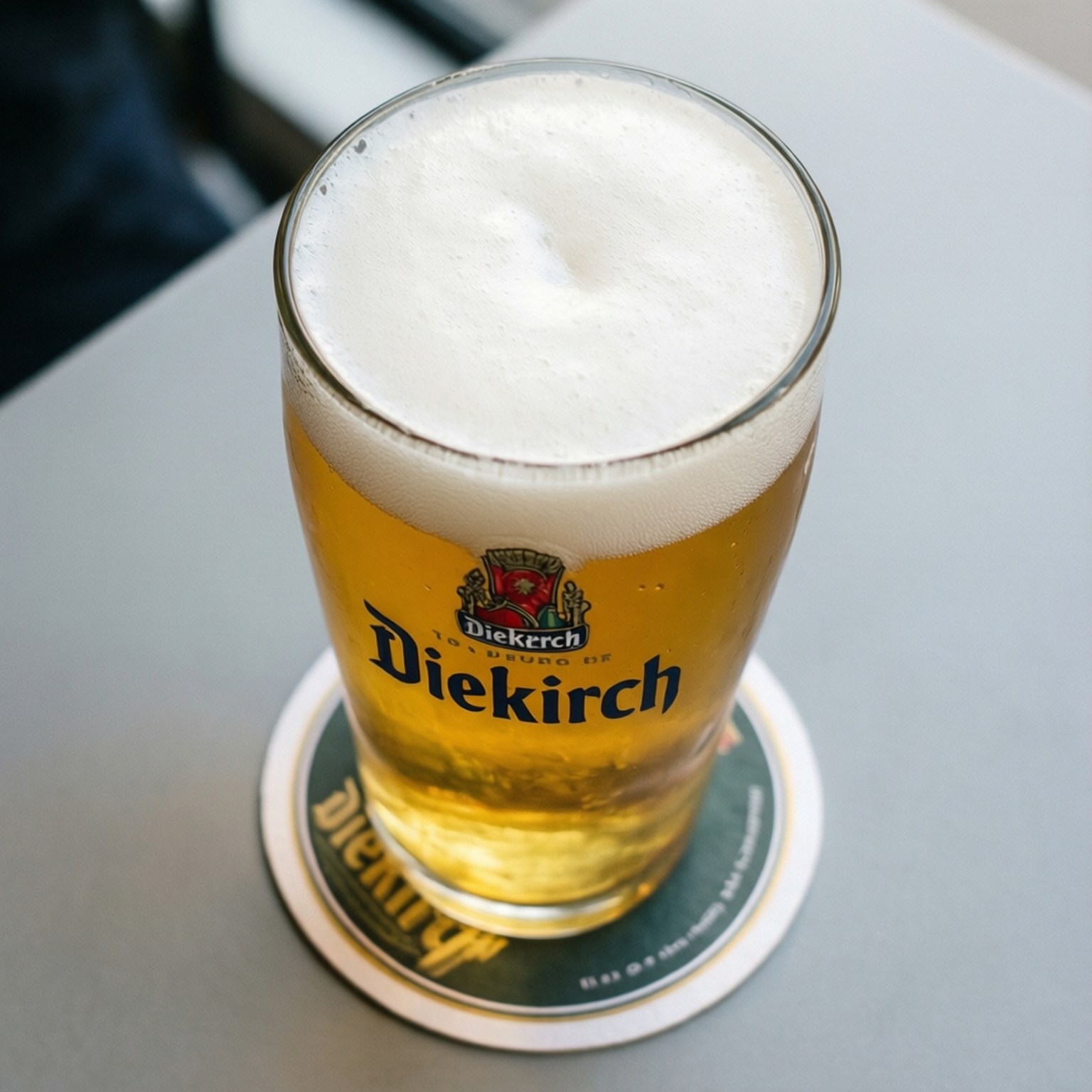 一杯 Diekirch 啤酒，有泡沫，放喺枱上嘅杯墊上。