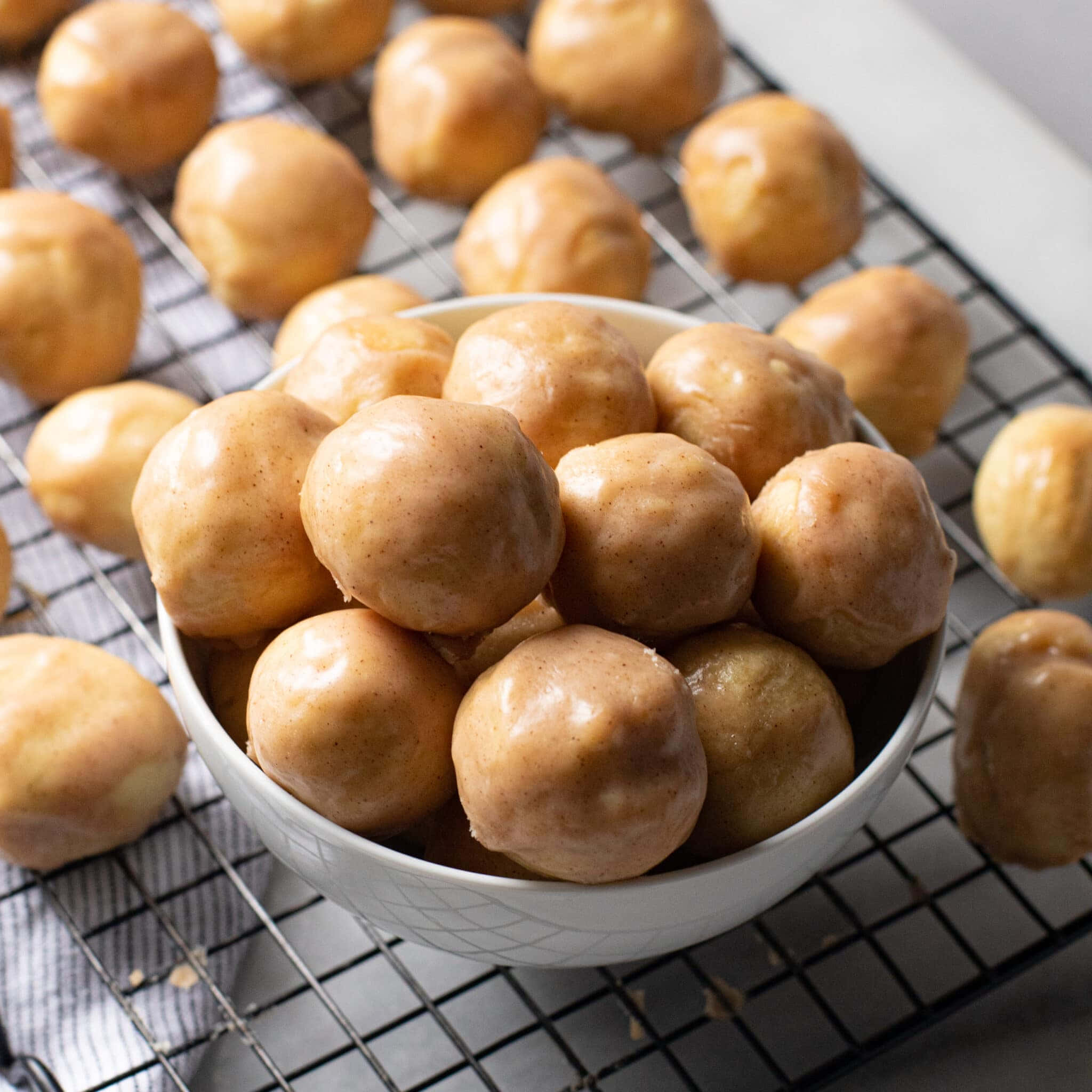Glazed Donut 桌布 壁紙 — 金色釉面冬甩球堆在白色碗中，放在冷卻架上，周圍散落更多。