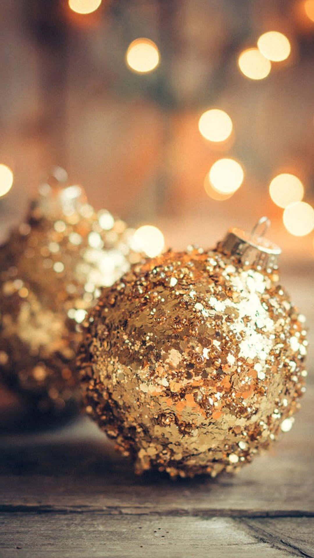 Rustic Christmas 桌布 壁紙 — 金色閃閃發光的聖誕裝飾品放置在質樸的木質表面上，背景有溫暖的散景燈光。