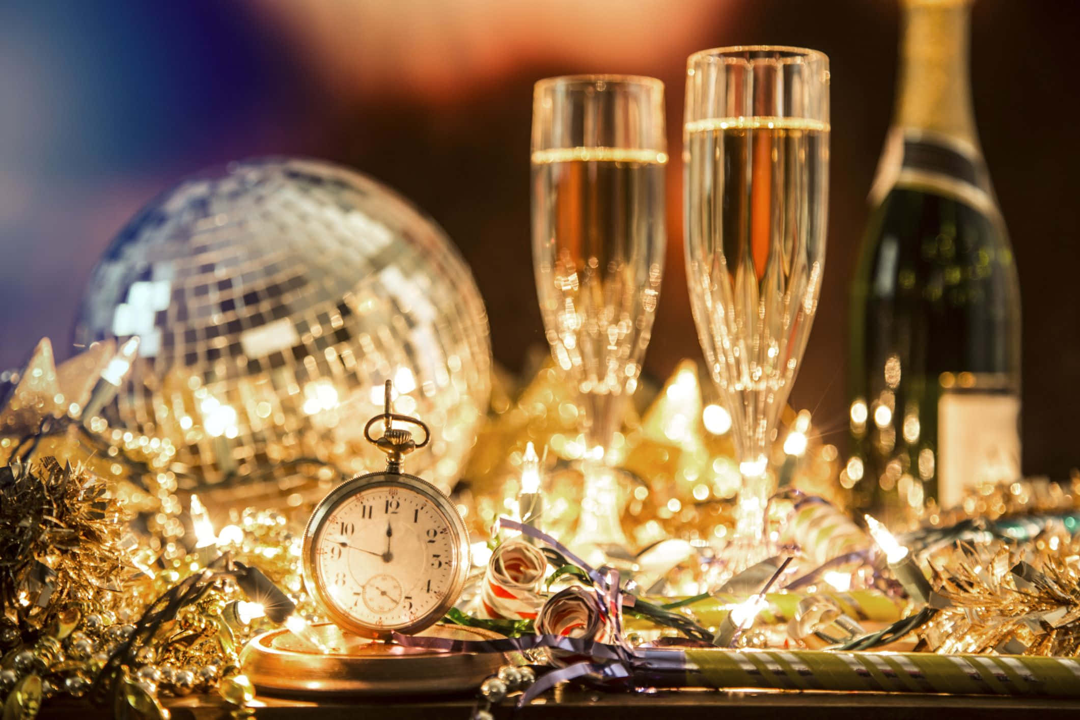 New Years Eve 桌布 壁紙 — 金色除夕慶祝，有香檳杯、迪斯科球和懷錶，在閃爍燈光和金屬彩帶中。