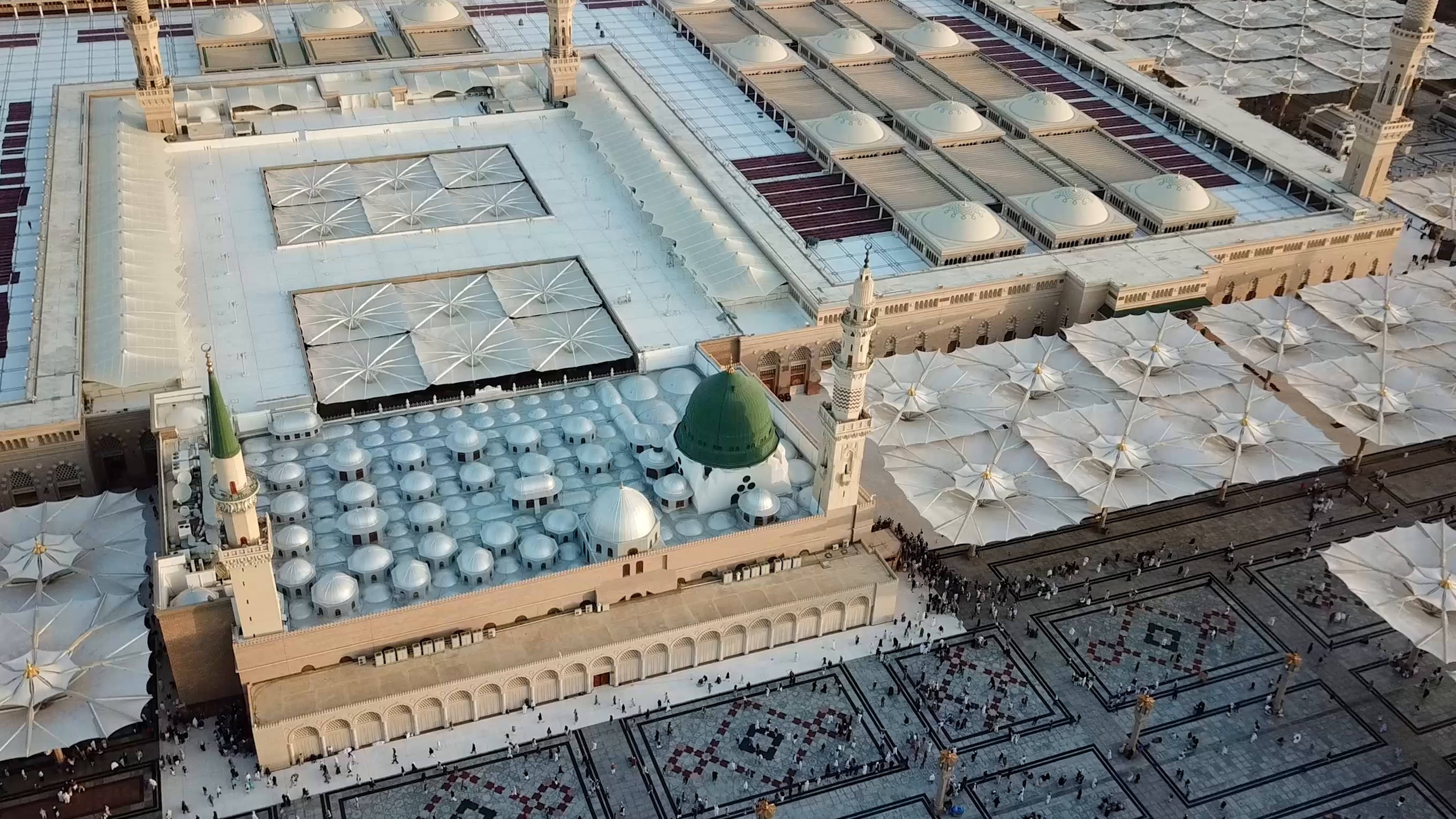 Madina Sharif 桌布 壁紙 — 金色陽光下，一個擁有綠色圓頂、白色帳篷和複雜瓷磚圖案的宏偉清真寺建築群的鳥瞰圖。