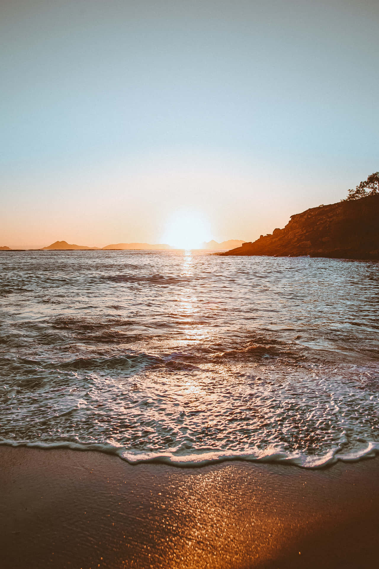 海上夕陽，沙灘上的海浪，遠方的懸崖