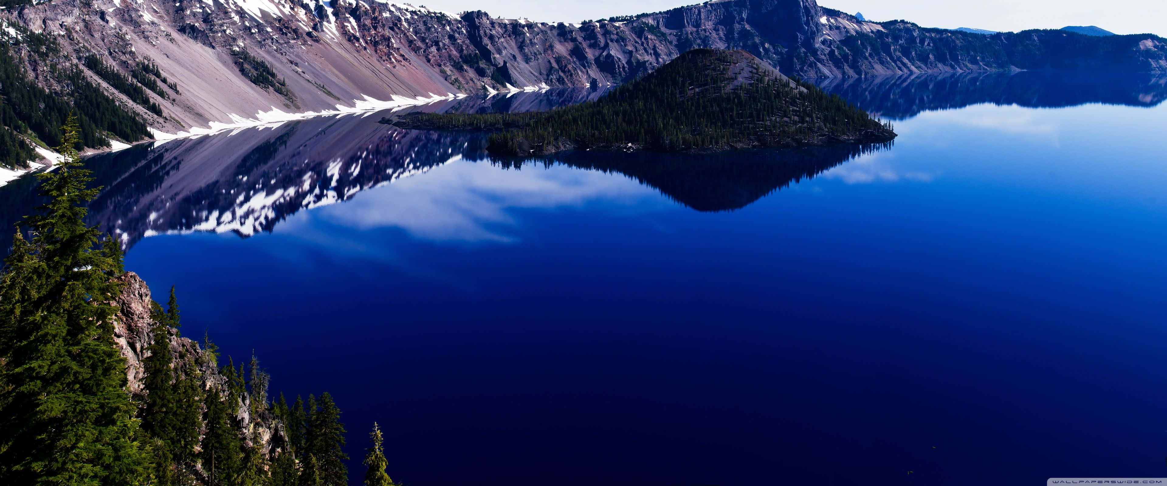 金蘋果盛放彩色光芒 壁紙 — 火山口湖的壯麗全景，深藍色的湖水完美地映照出白雪覆蓋的山脈和常綠森林。