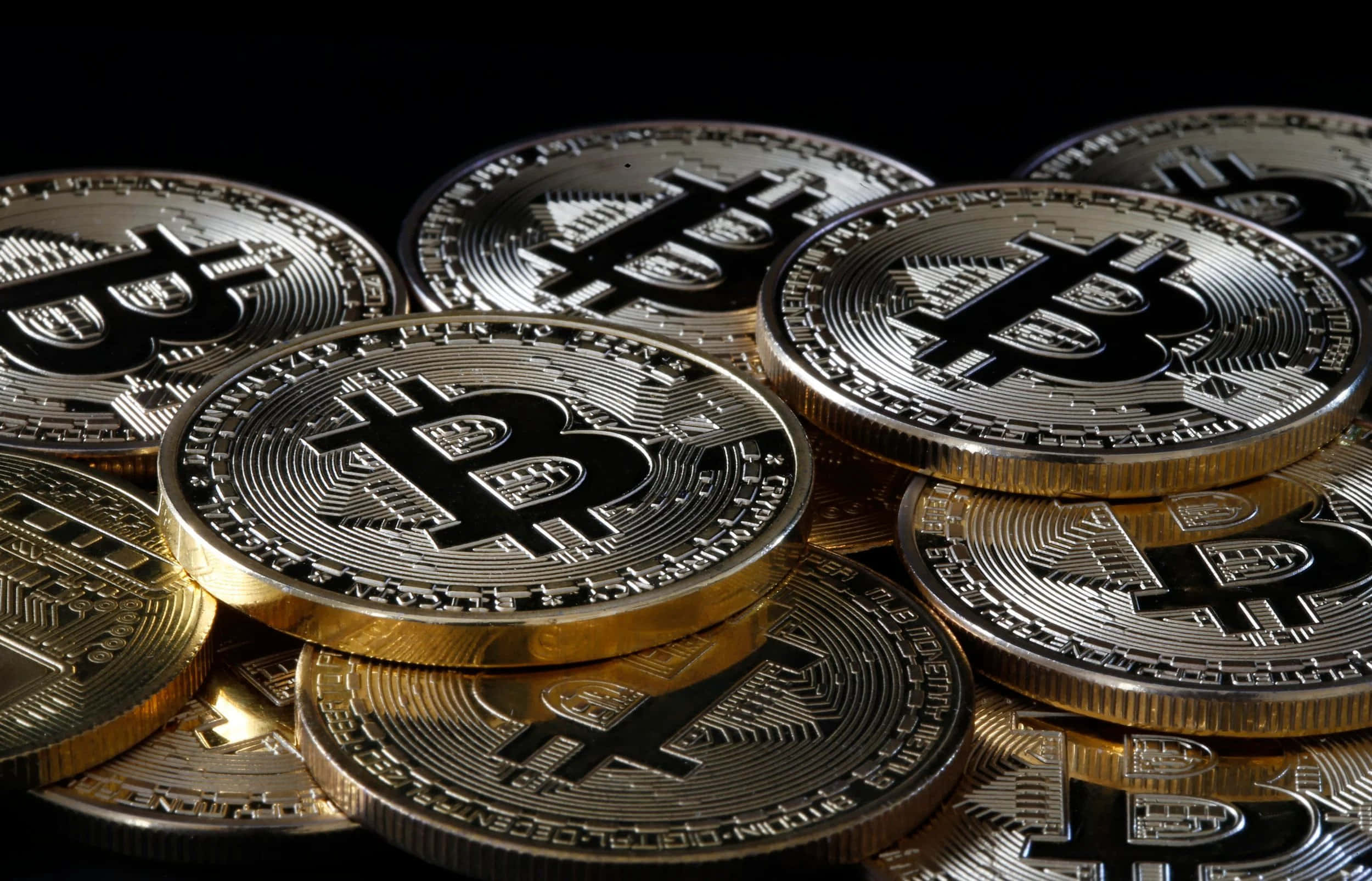 金融的未來：比特幣 壁紙 — 閃亮的金色比特幣堆疊在黑色背景上，帶有反射高光。
