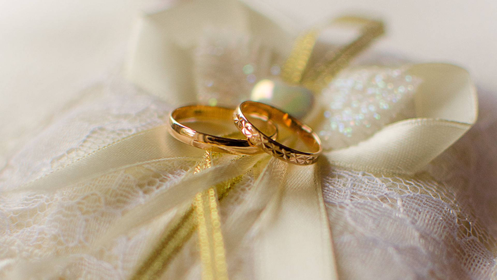 兩枚金色結婚戒指放在蕾絲和絲帶裝飾上。