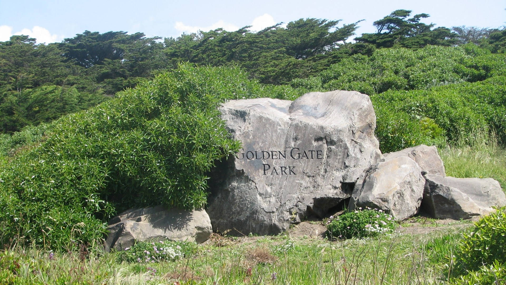 一個金門公園的石質標誌，周圍環繞著綠色植物和樹木。