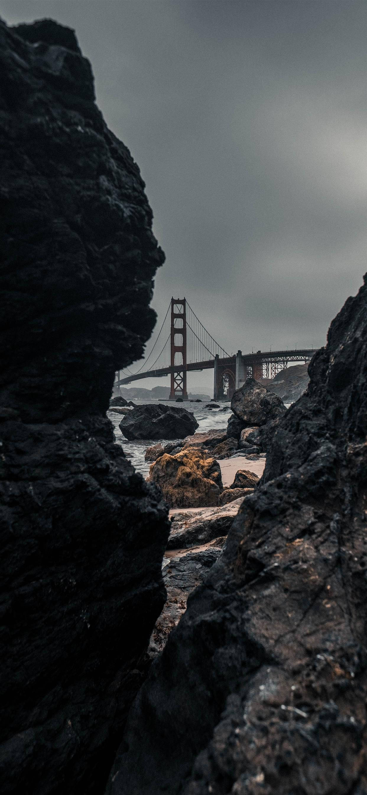 San Francisco Phone 桌布 壁紙 — 金門大橋從狹窄岩石裂縫中觀看，下方是陰沉灰暗的天空和拍岸的浪花。