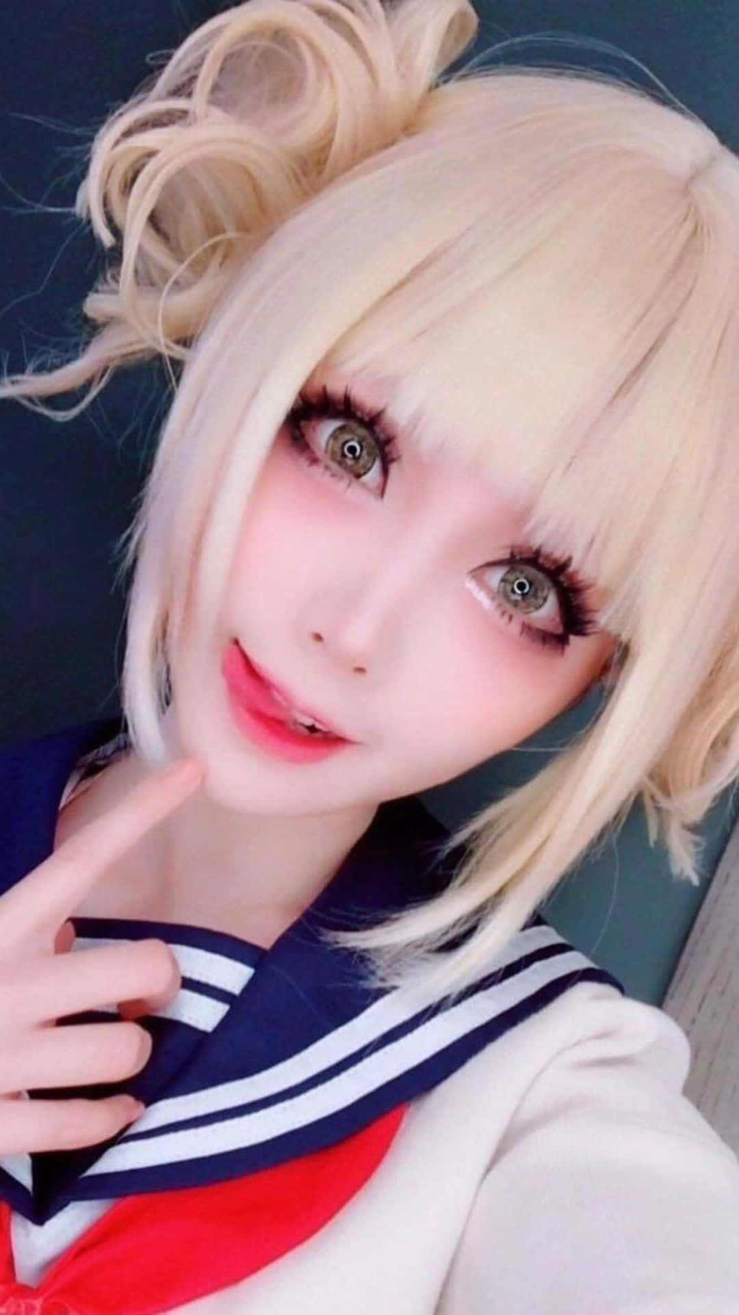 Cosplay Anime Kawaii 桌布 壁紙 — 金髮動漫風格角色扮演者的特寫，身穿水手服，妝容明亮，手指做出俏皮姿勢。