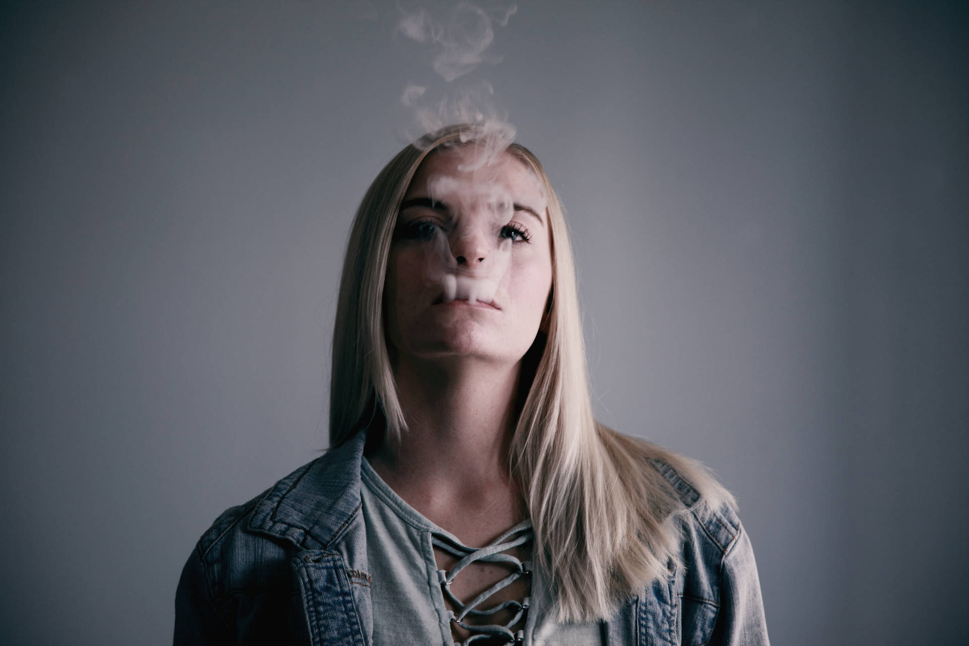 年輕女性在灰色背景的攝影棚中呼出蒸氣。