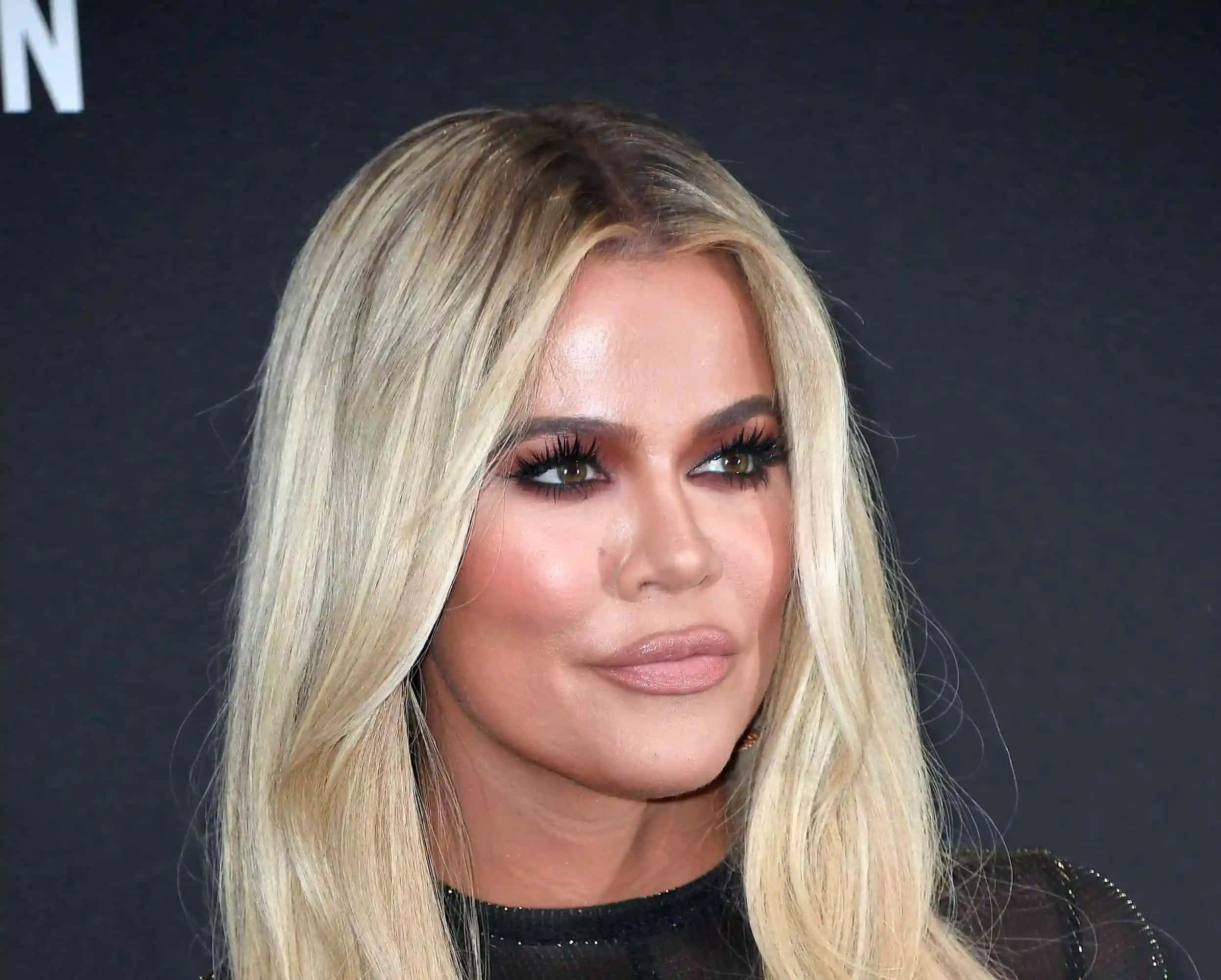 Khloe Kardashian 桌布 壁紙 — 金髮女性嘅特寫肖像，擁有戲劇性嘅睫毛同柔和化妝，背景係深色。