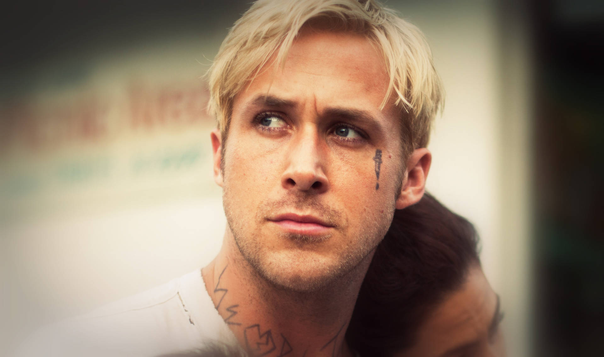 金髮男子臉頰上有淚珠紋身，表情嚴肅地向上望。