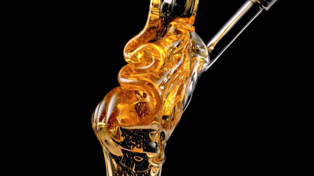 金黃色的蜂蜜從玻璃滴管中滴落在黑色背景上。