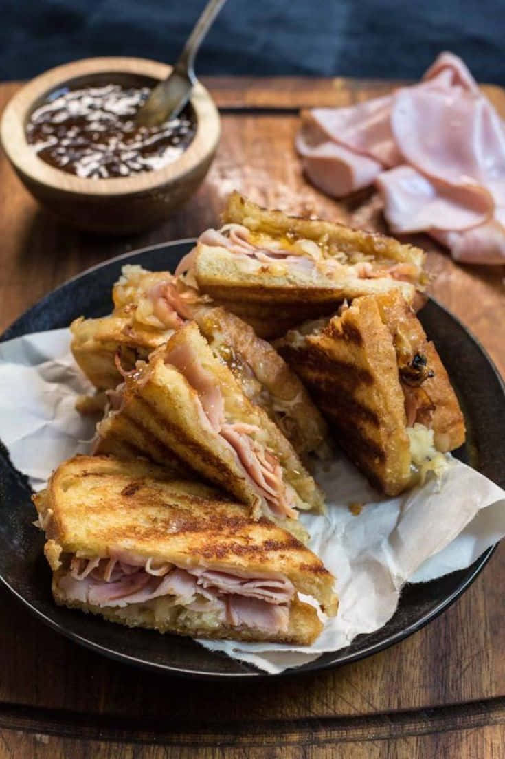 Black Forest Ham 桌布 壁紙 — 金黃色烤火腿芝士三文治切成三角形放在深色碟上，配上蘸醬。