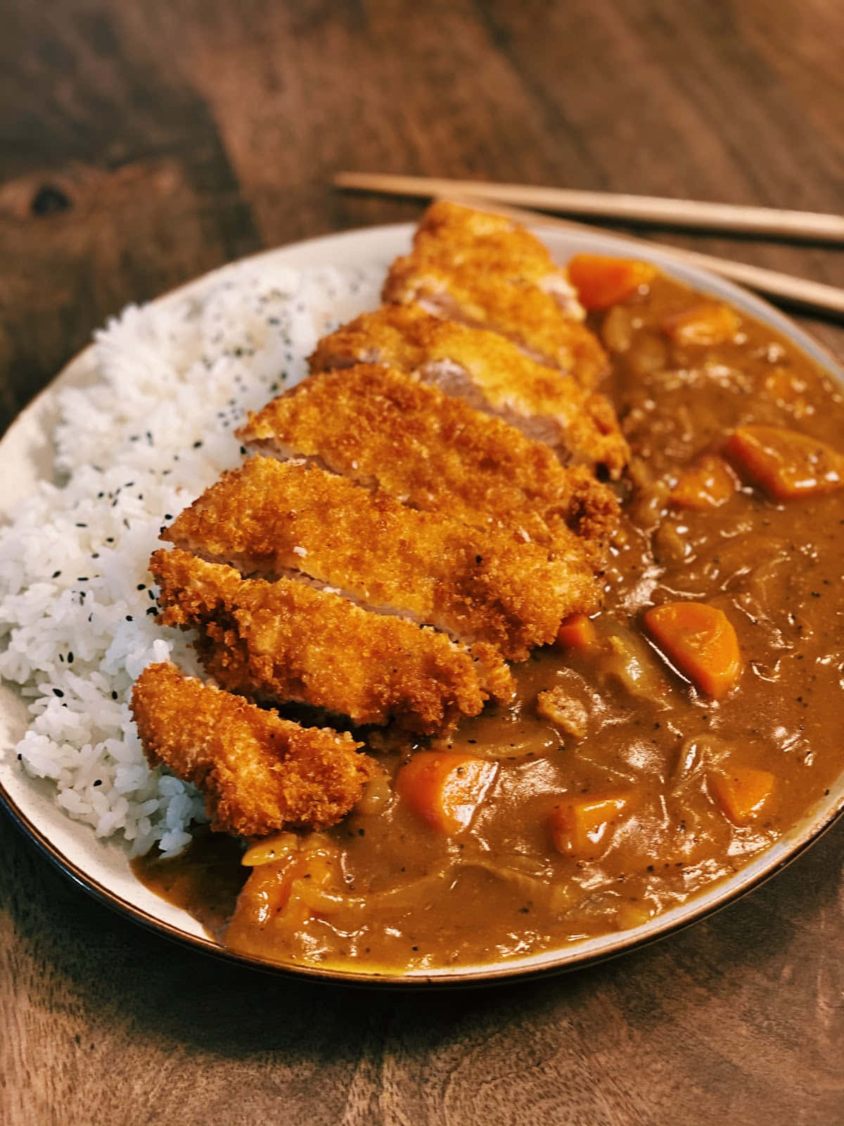 Japanese 桌布 壁紙 — 金黃色的切片吉列豬扒放在濃郁的棕色咖喱中，旁邊是白飯，置於木桌上。