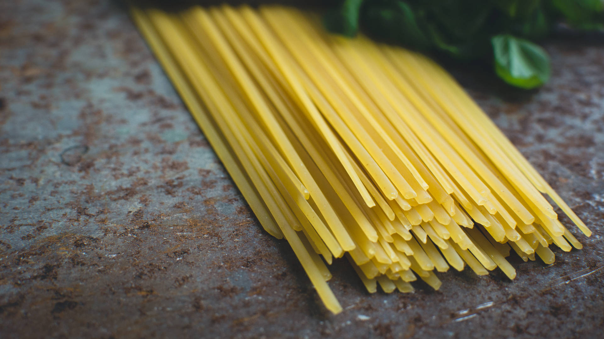 Pasta 桌布 壁紙 — 金黃色的未煮熟意大利麵條放在經風化的鏽蝕金屬表面上，附近有新鮮的羅勒葉。