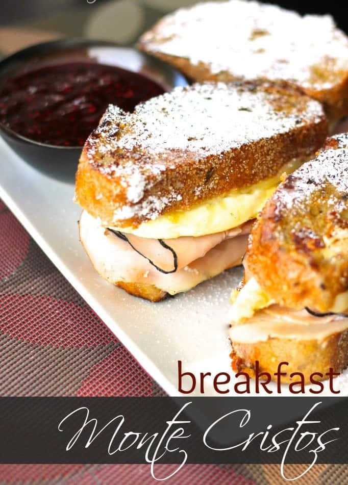 Black Forest Ham 桌布 壁紙 — 金黃色的烤蒙特克里斯托三文治撒上糖粉，放在碟上，旁邊有一小碗深色雜莓果醬。