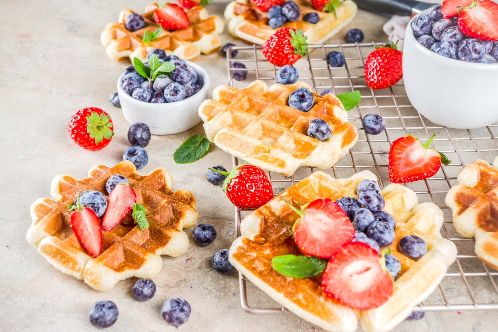 Waffle 桌布 壁紙 — 金黃色的窩夫，上面放著新鮮草莓、藍莓和薄荷葉，在金屬架上冷卻。