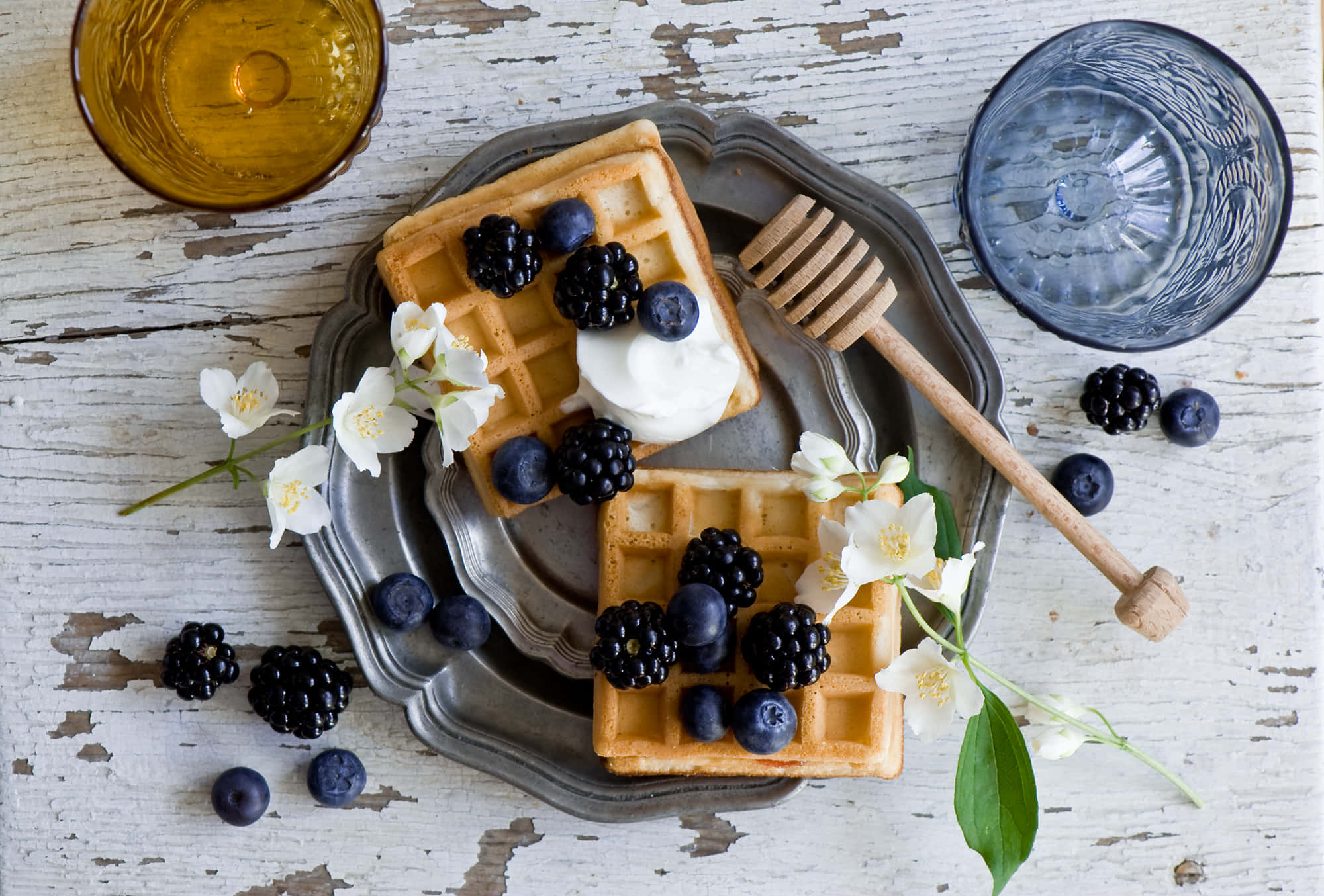 Waffle 桌布 壁紙 — 金黃色的窩夫上面放著黑莓、藍莓和乳酪，放在一個暗淡的銀盤上，旁邊有蜂蜜棒和玻璃器皿，放在一個風化的白色木質表面上。