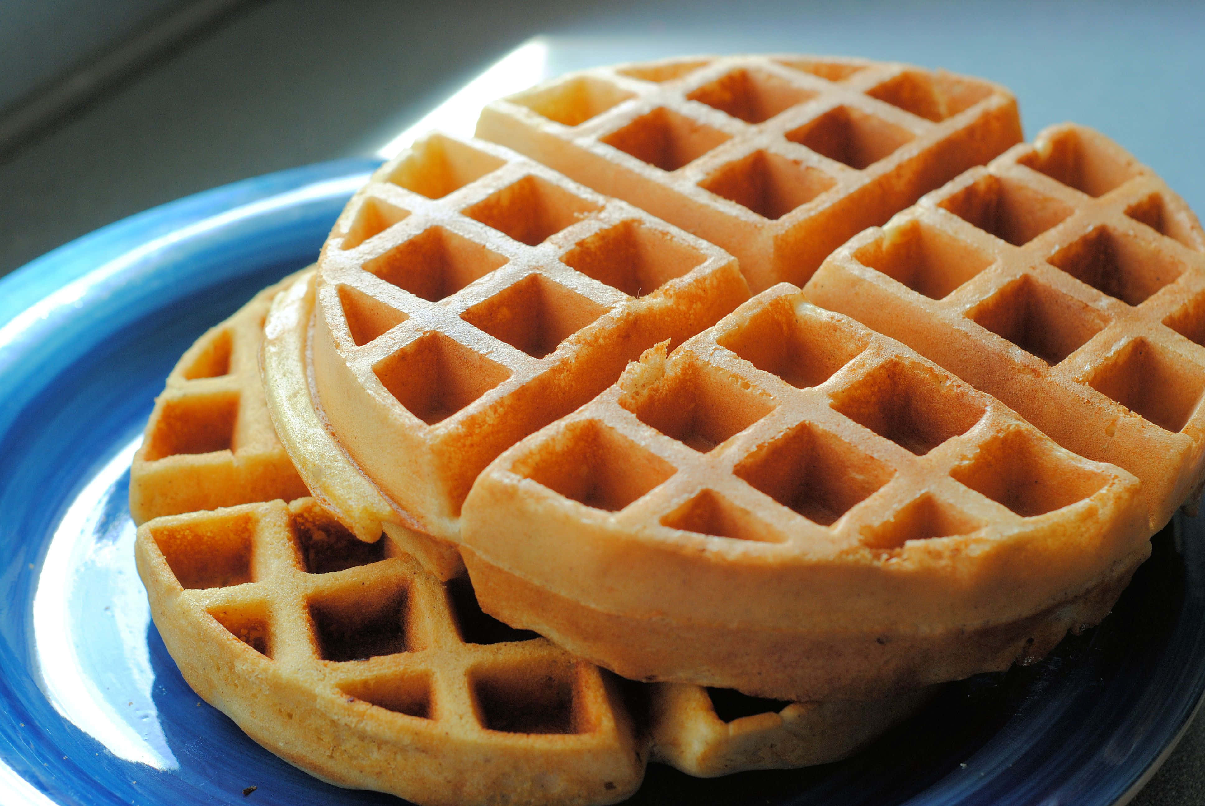 Waffle 桌布 壁紙 — 金黃色的窩夫疊放在鮮藍色的碟子上，柔和晨光突顯其酥脆質感。