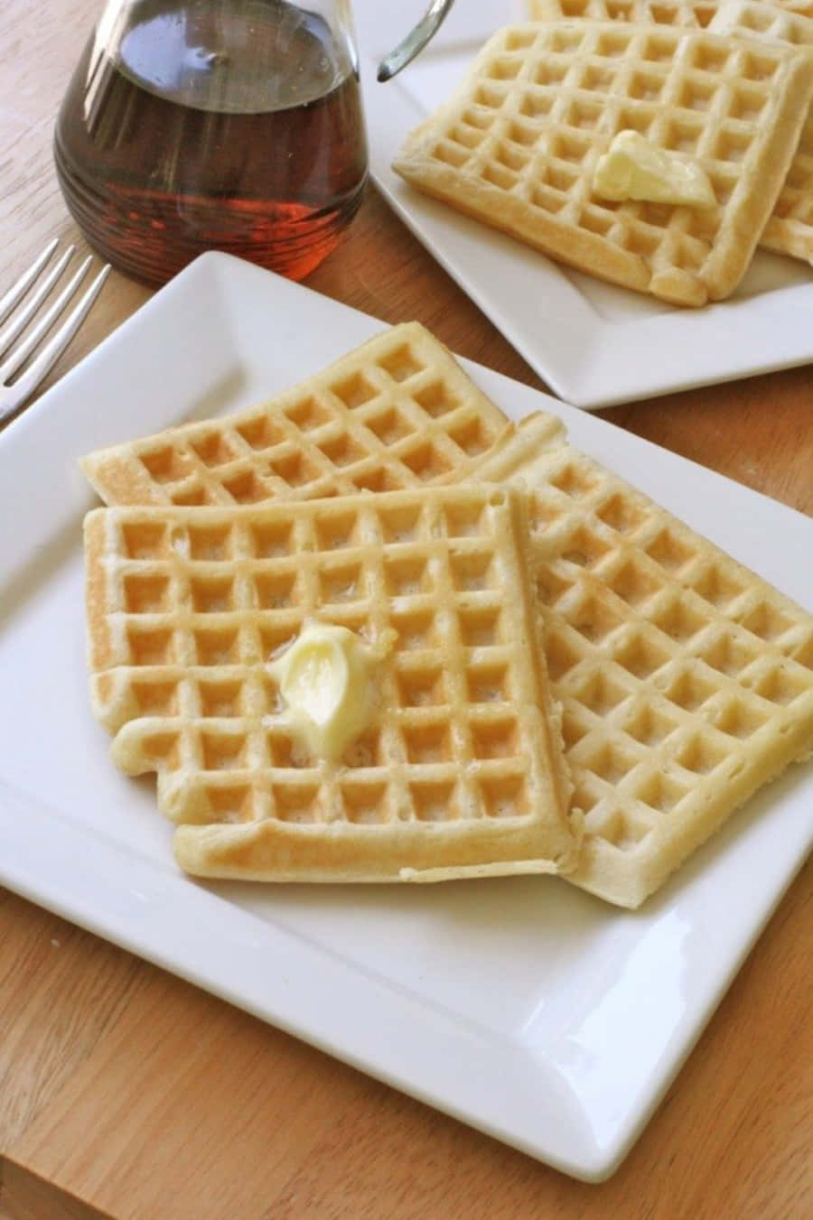 Waffle 桌布 壁紙 — 金黃色的窩夫配上融化的牛油和糖漿，放在白色碟子上，置於溫暖的木桌上，令人垂涎。