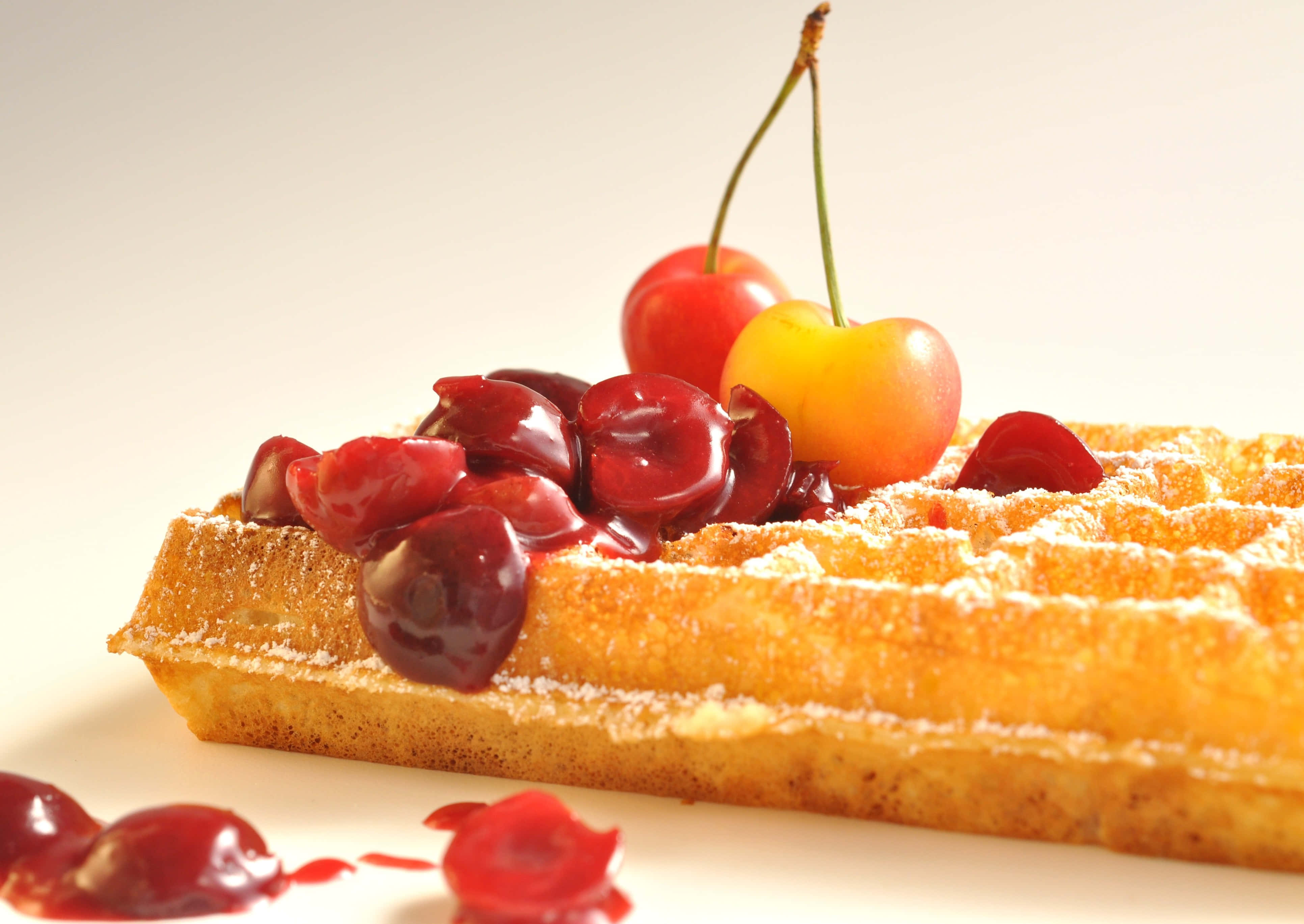 Waffle 桌布 壁紙 — 金黃色窩夫撒上糖粉，上面放有光澤的櫻桃和糖漿，背景為純白色。