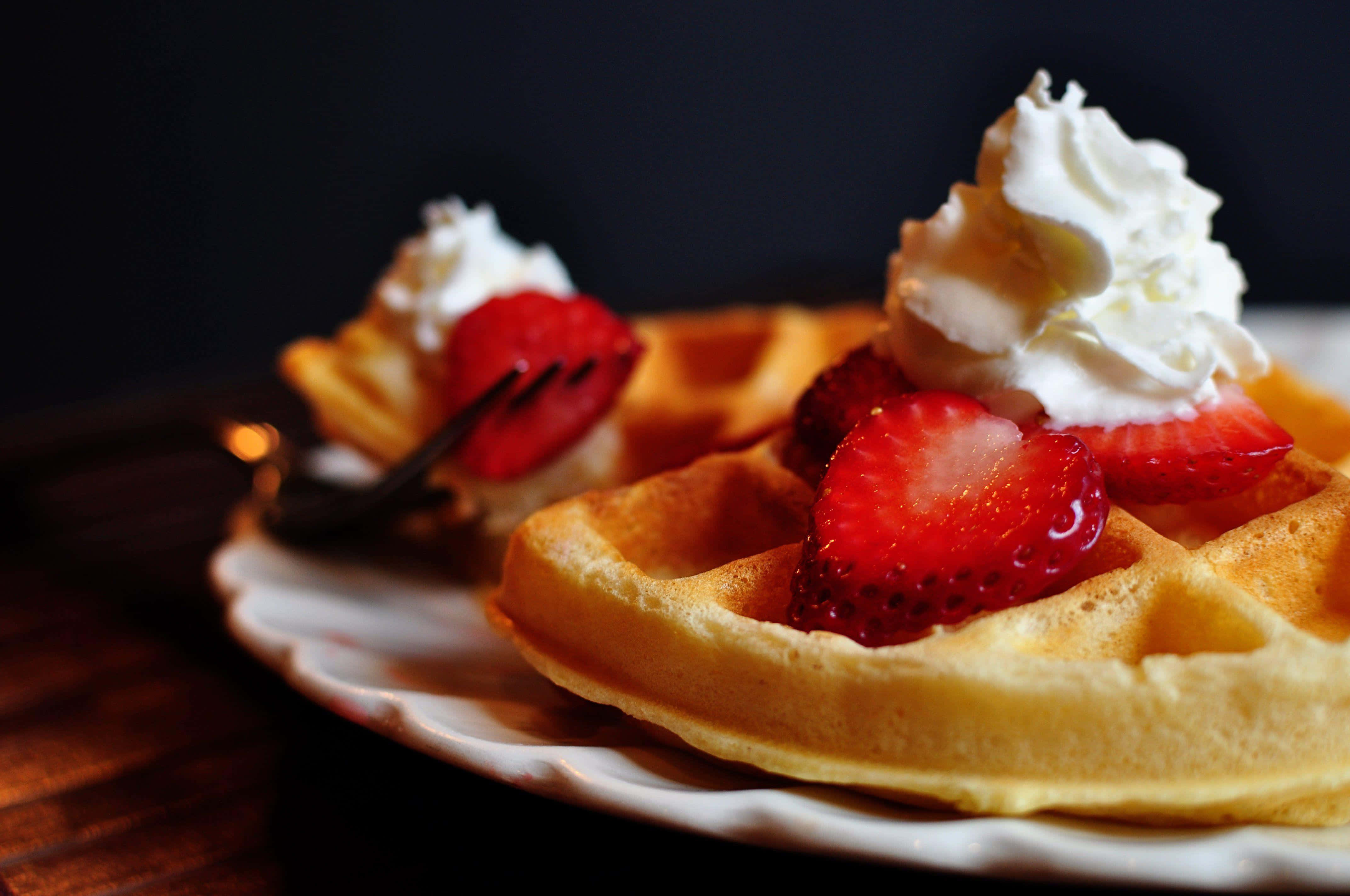 Waffle 桌布 壁紙 — 金黃色窩夫配上新鮮草莓和忌廉，放在白色碟上，深色背景襯托下格外誘人。