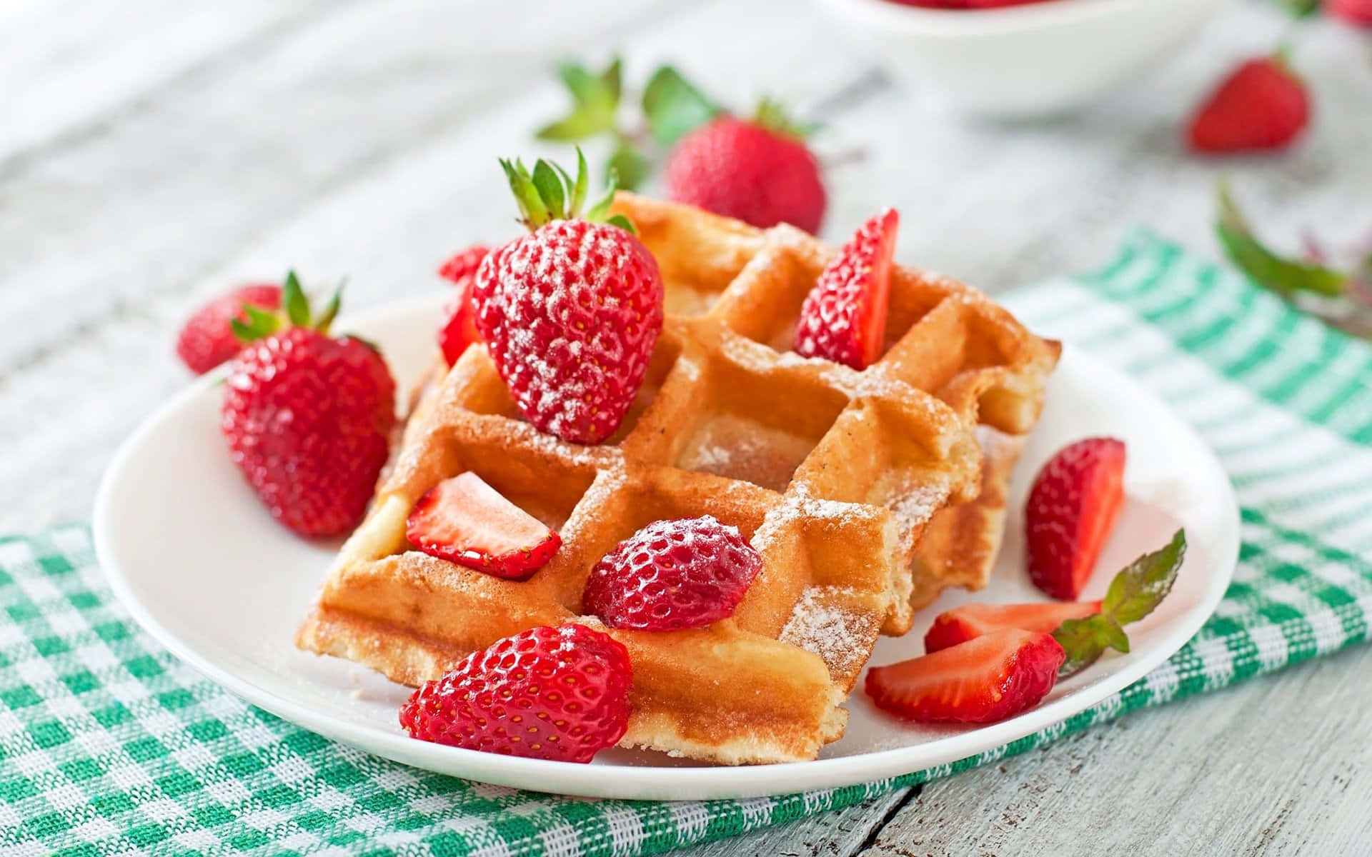 Waffle 桌布 壁紙 — 金黃色窩夫配上新鮮草莓和糖粉，置於格仔餐巾上。