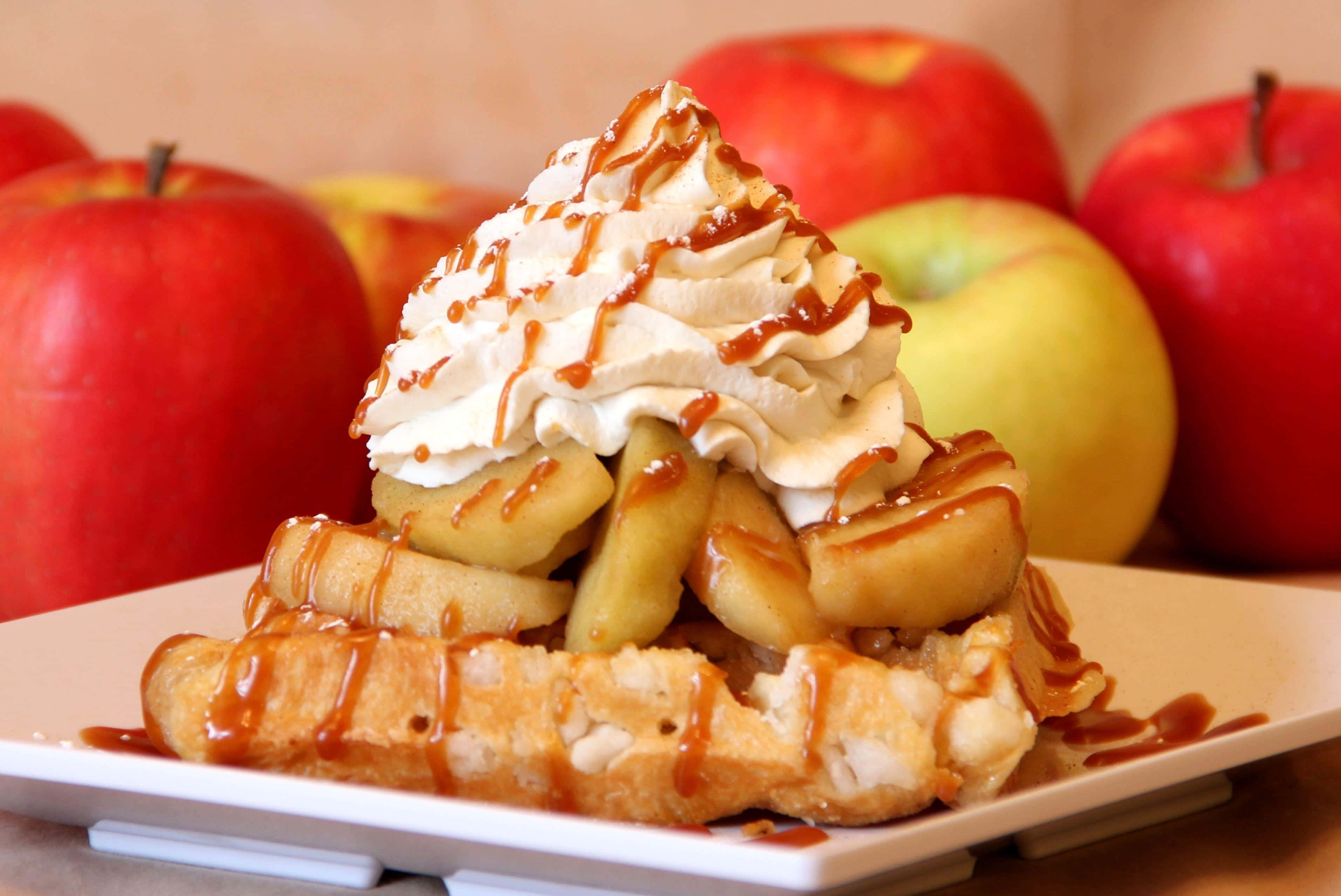 Waffle 桌布 壁紙 — 金黃色窩夫配上焦糖蘋果片、鮮奶油和焦糖醬，周圍環繞著新鮮的紅蘋果和青蘋果。