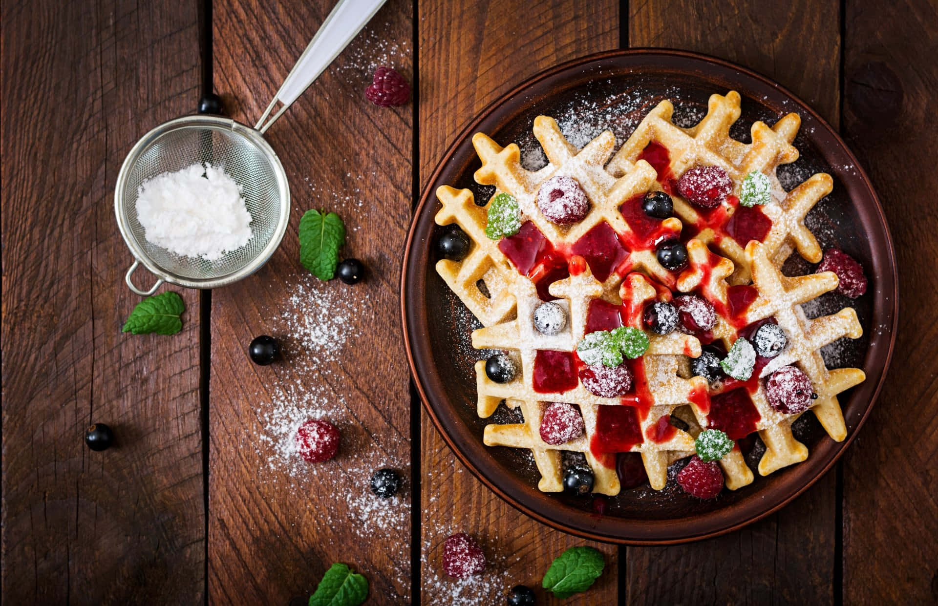 Waffle 桌布 壁紙 — 金黃色窩夫配上莓果、薄荷和糖粉，放在質樸的木桌上，旁邊有一個篩糖器。