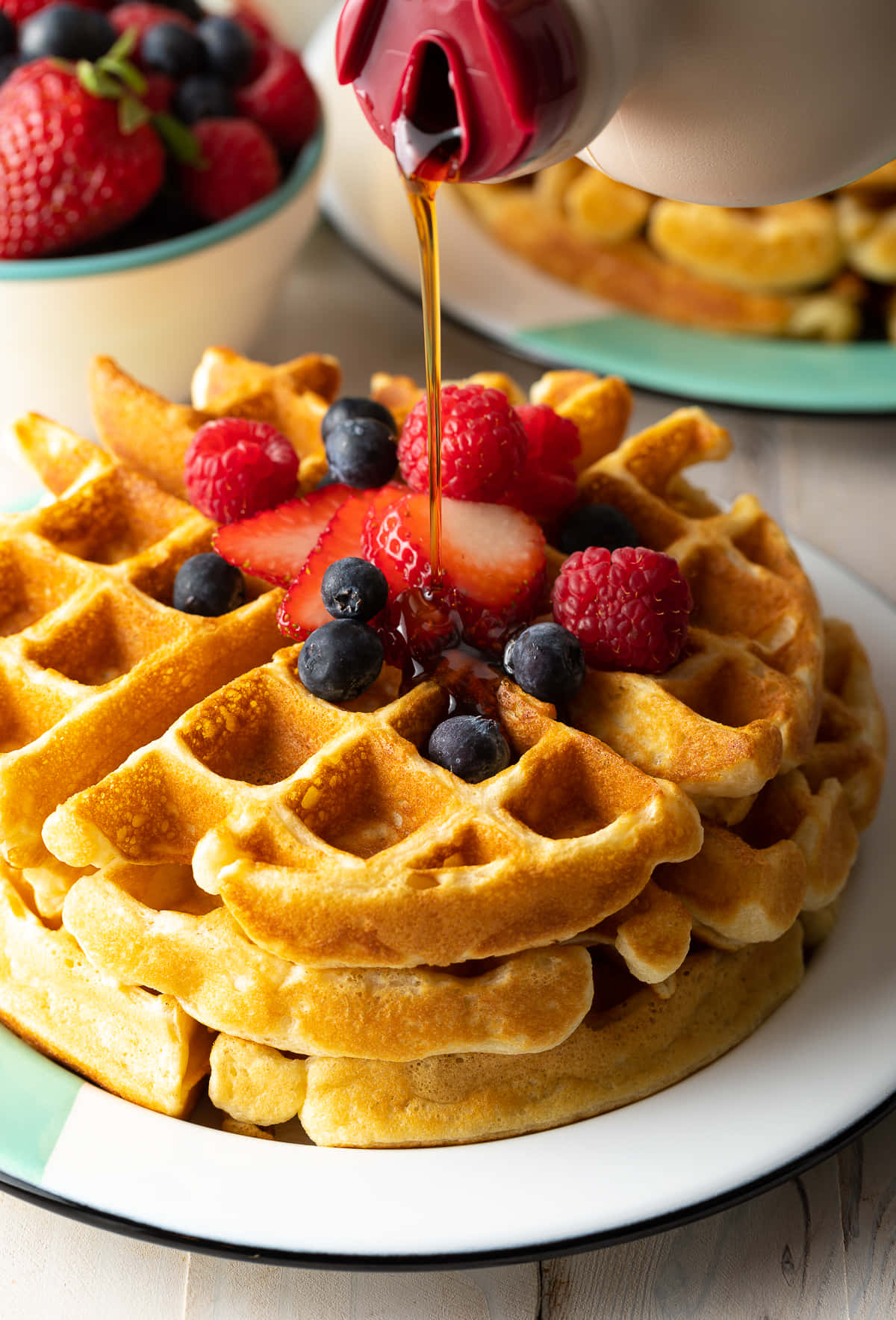Waffle 桌布 壁紙 — 金黃色窩夫高高疊起，上面放滿新鮮莓果，糖漿正在淋下，特寫鏡頭。